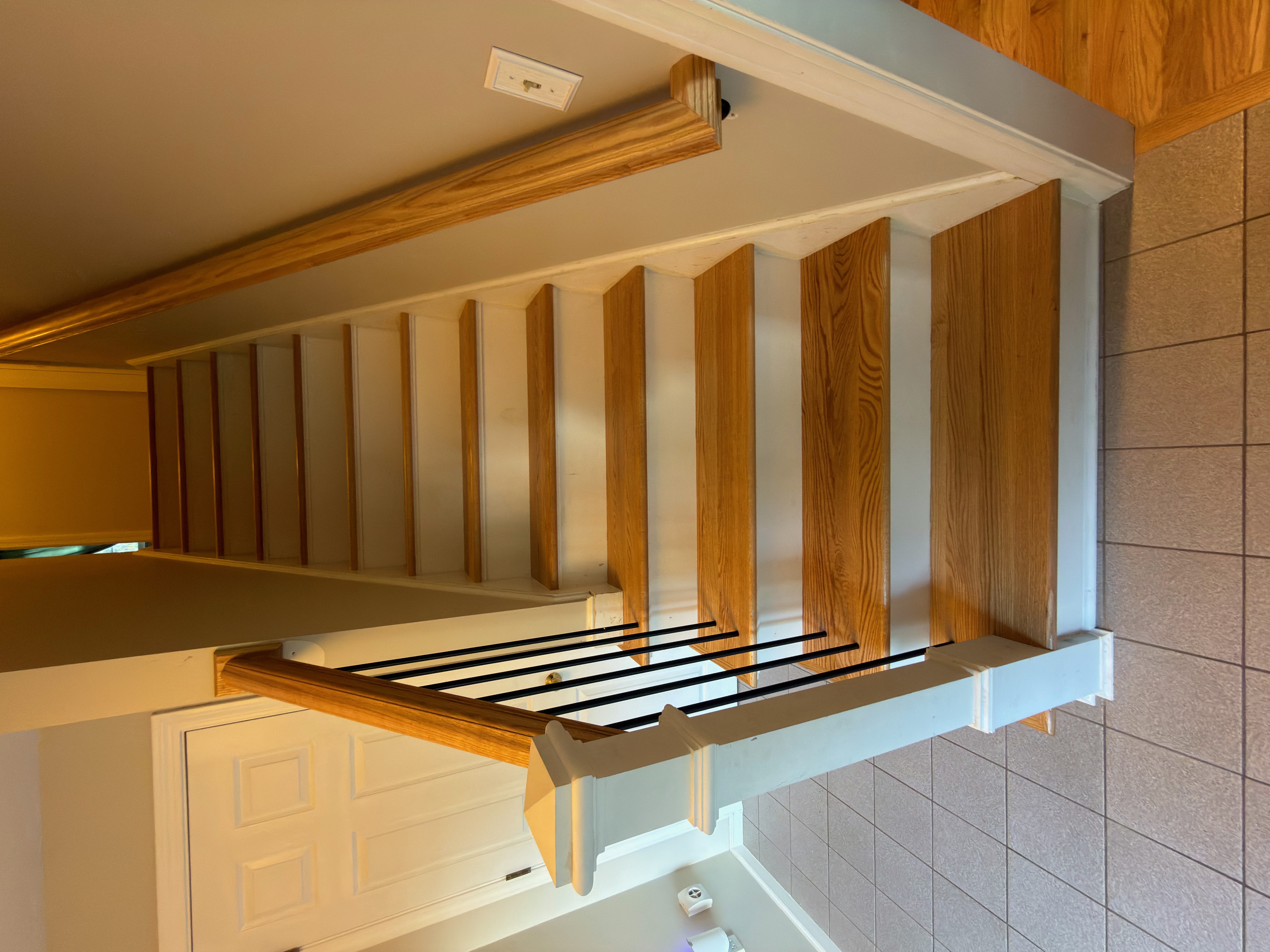 Wrentham MA — finished staircase from bottom looking up showing full run of new red oak treads, white risers, black metal balusters, and new hardwood hallway above