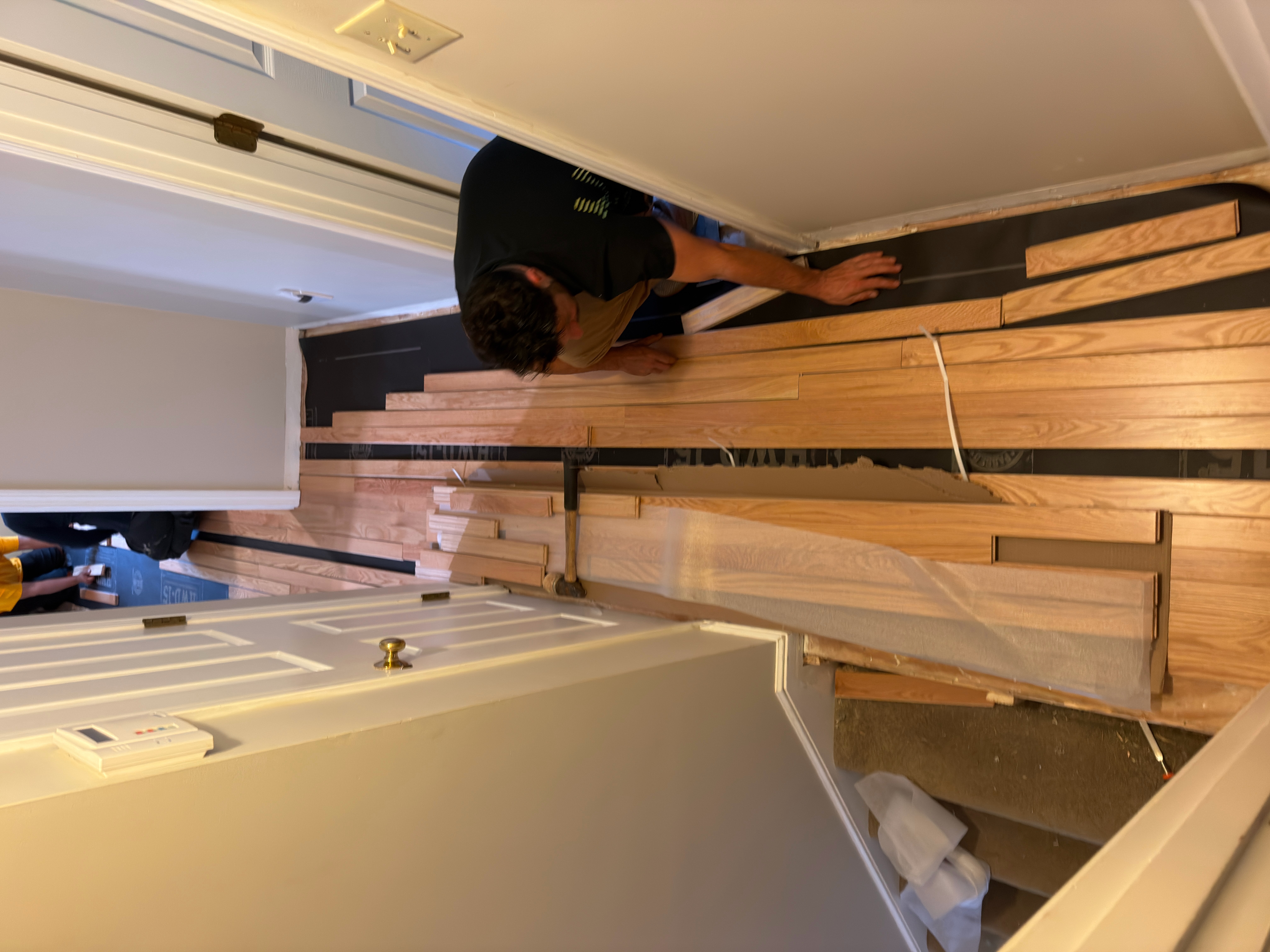 Wrentham MA — crew installing prefinished red oak in hallway with bedroom doorway visible