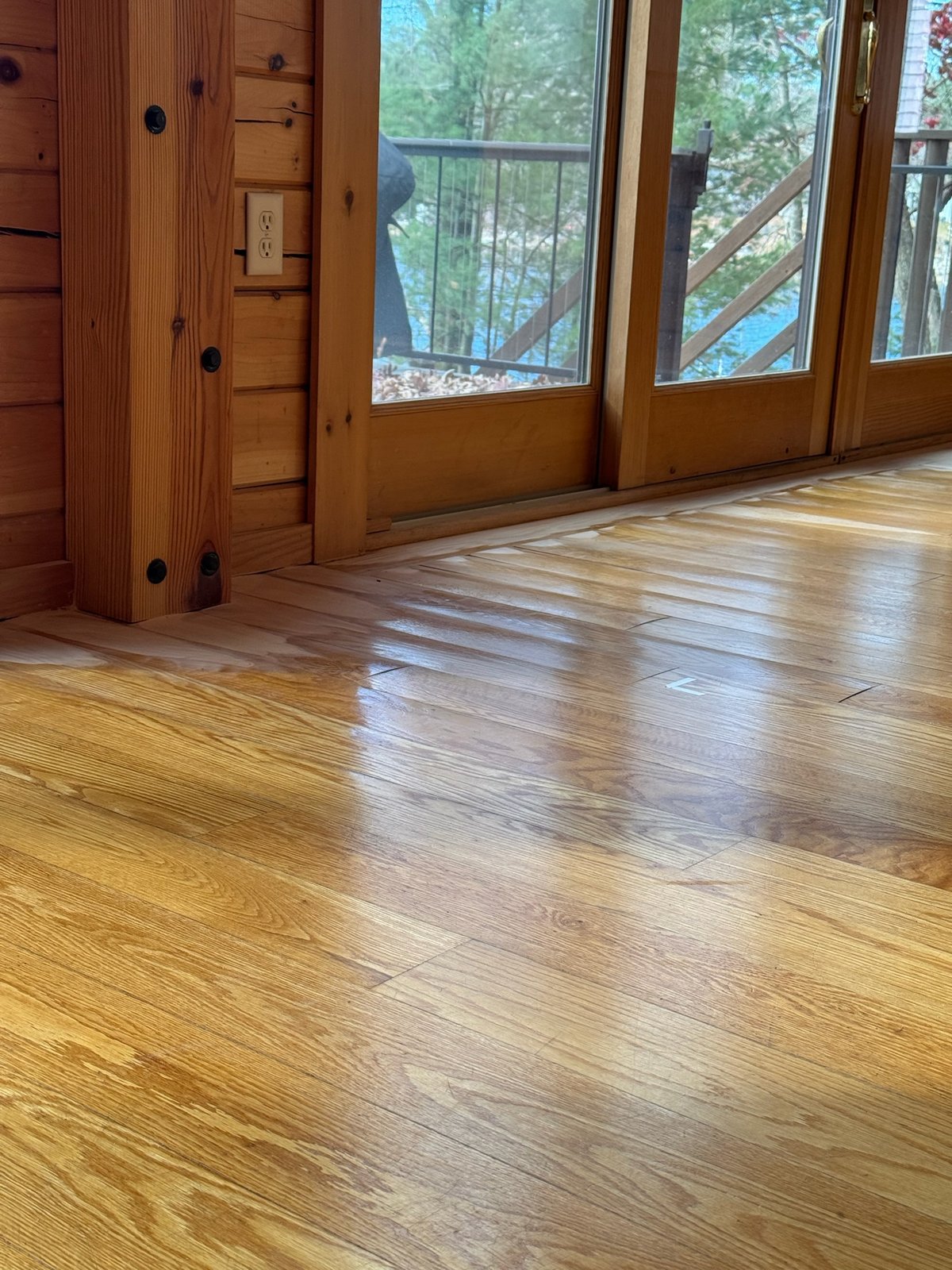 Killingly CT — lakefront cabin interior showing the lake through a glass door with light-colored hardwood floor and visible damage in front of the door
