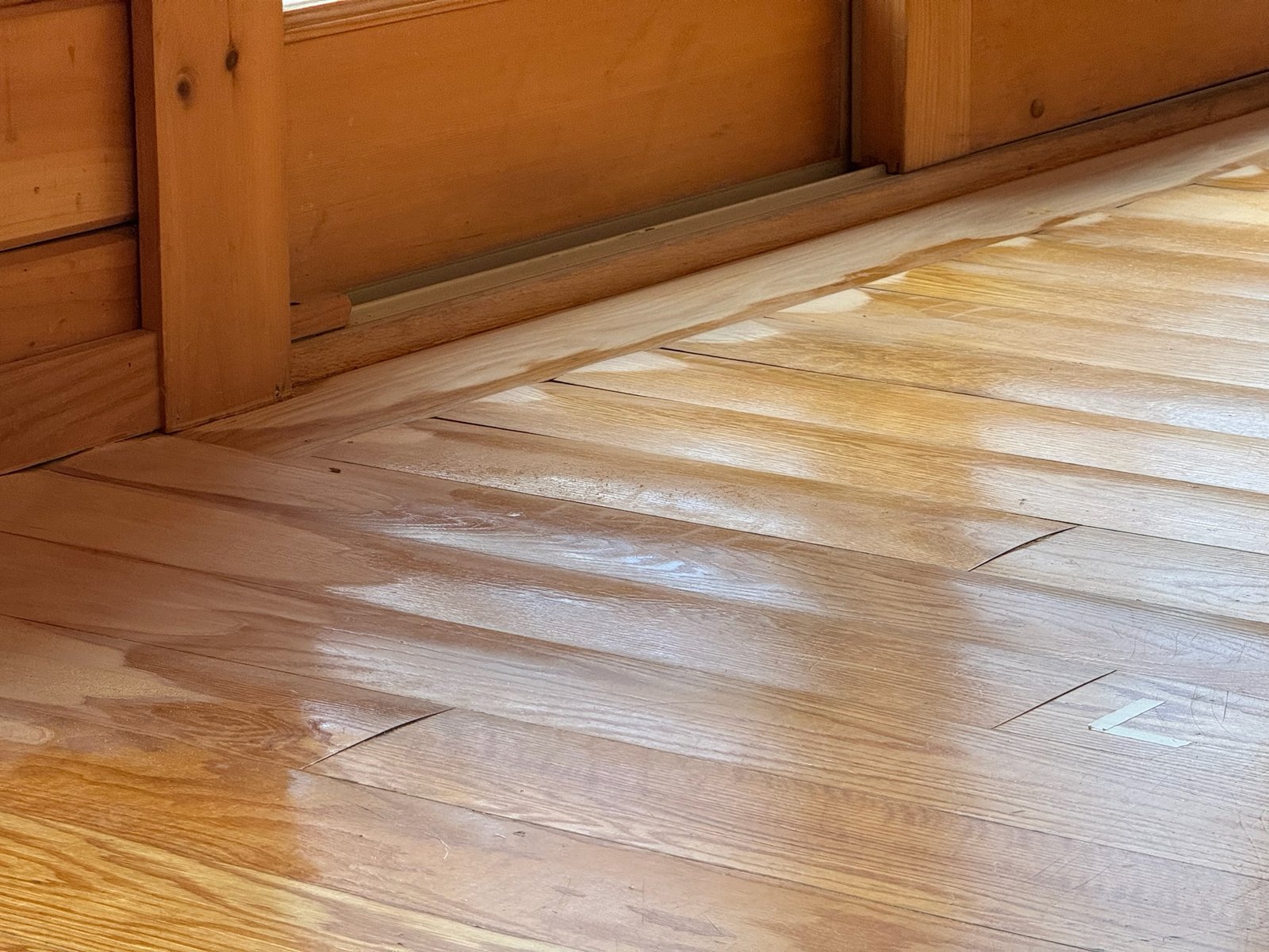 Killingly CT lake cabin — water-damaged hardwood with irregular light-colored staining and gaps between planks before restoration
