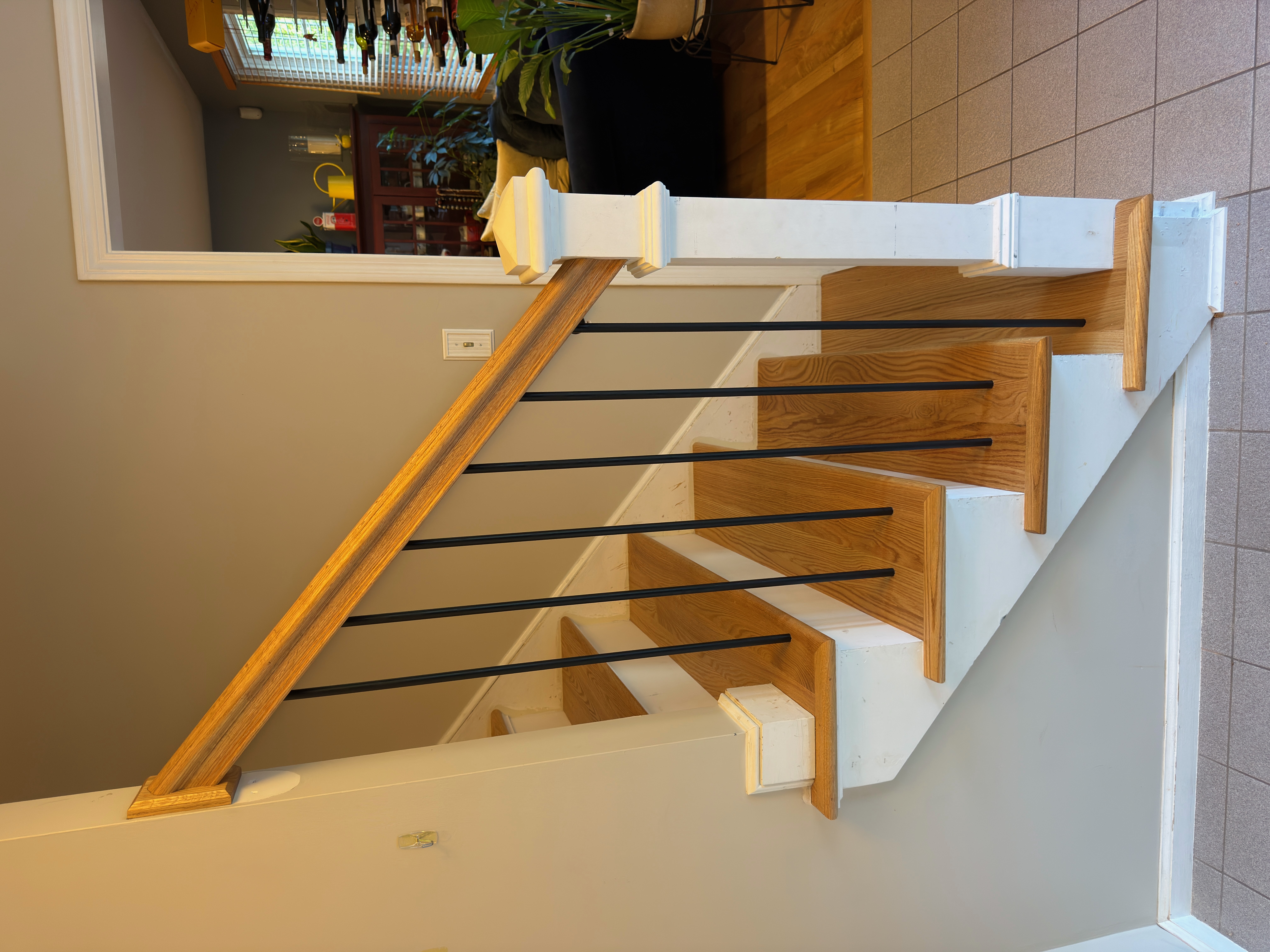 Wrentham MA — finished staircase detail showing square white newel post, black metal balusters, and wood handrail