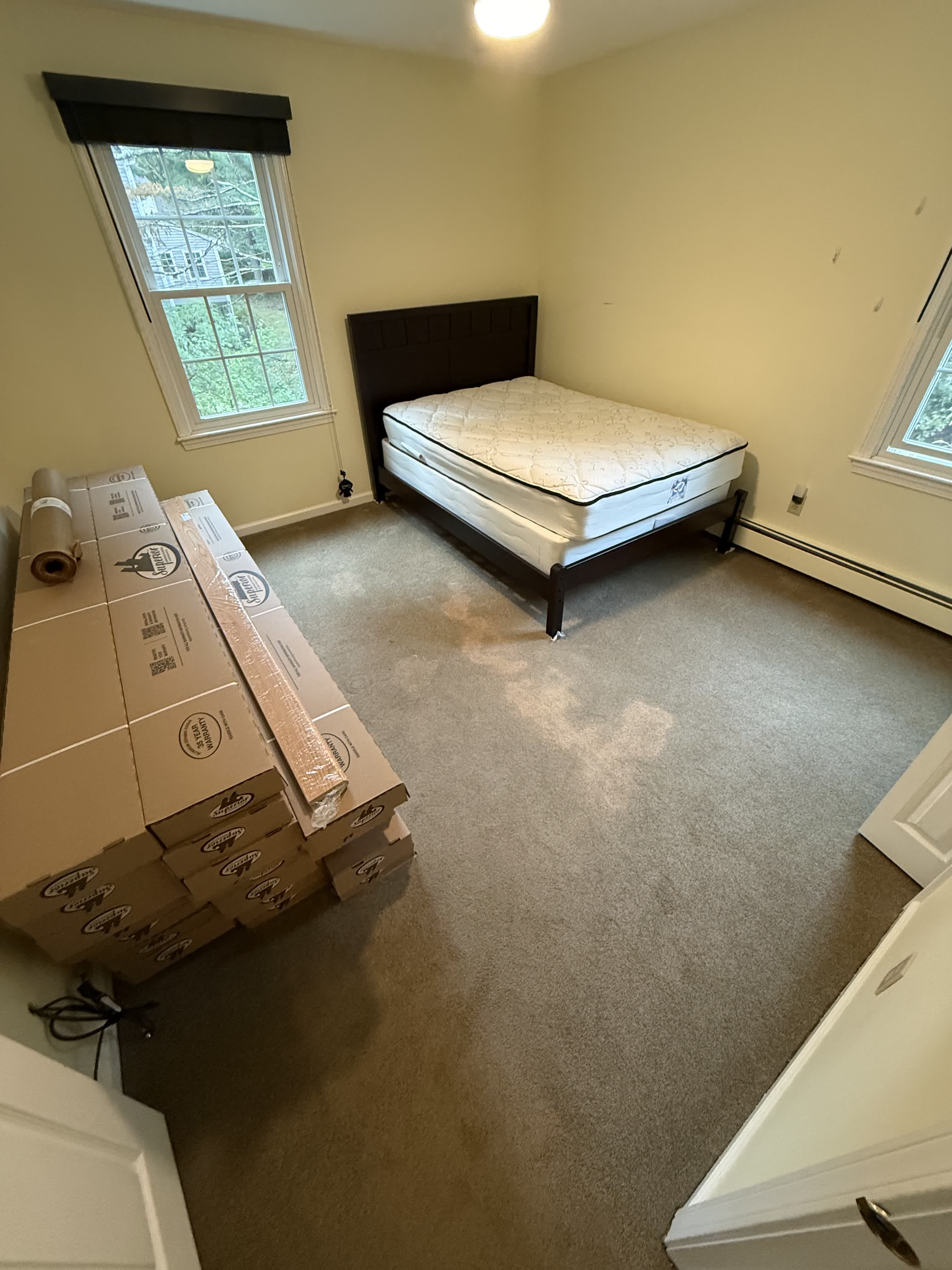 Wrentham MA — smaller bedroom with existing carpet and prefinished red oak flooring boxes staged for installation