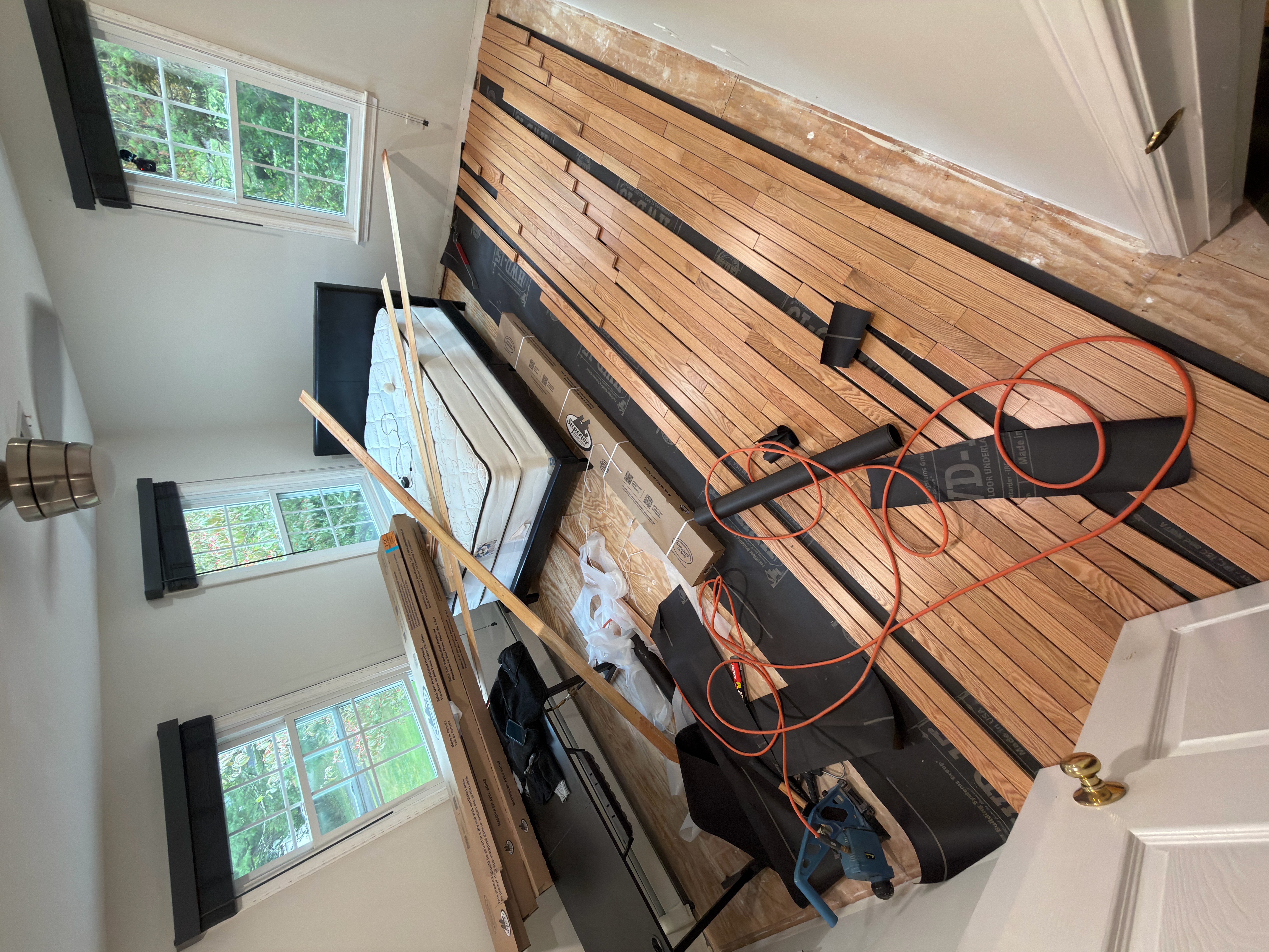 Wrentham MA — flooring installation progress across bedroom floor with underlayment and tools visible