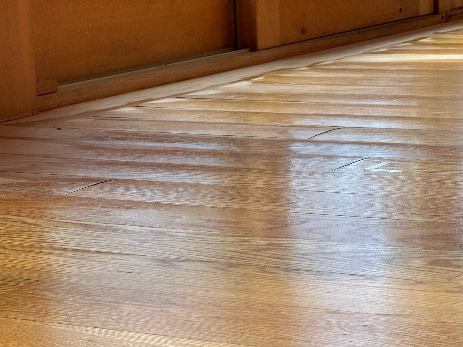 Killingly CT lake cabin — water-damaged hardwood showing warped and buckled planks, gaps between boards, and a diagonal crack before restoration
