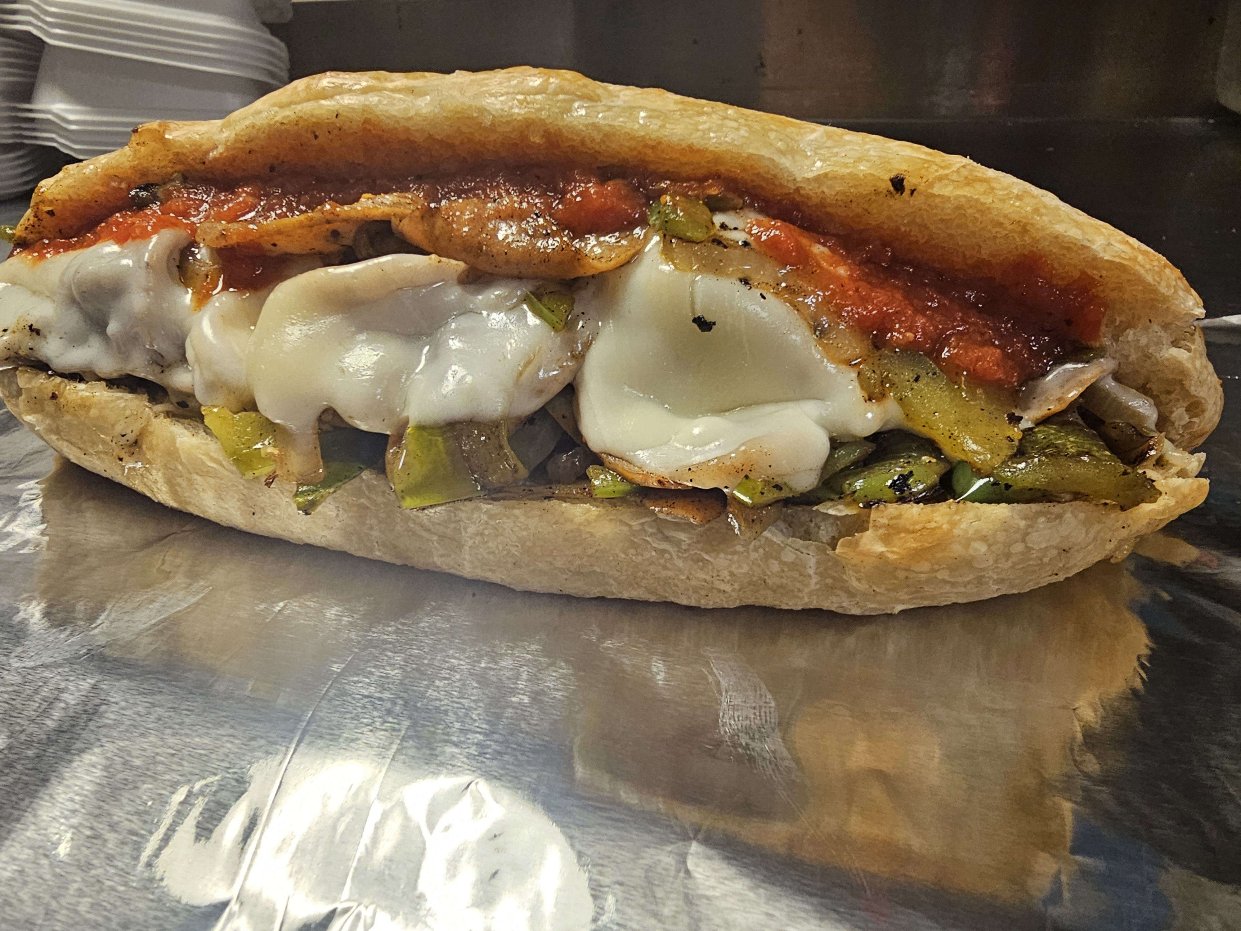 Cheesesteak with peppers, onions, melted cheese and sauce on a crusty JoJo's roll