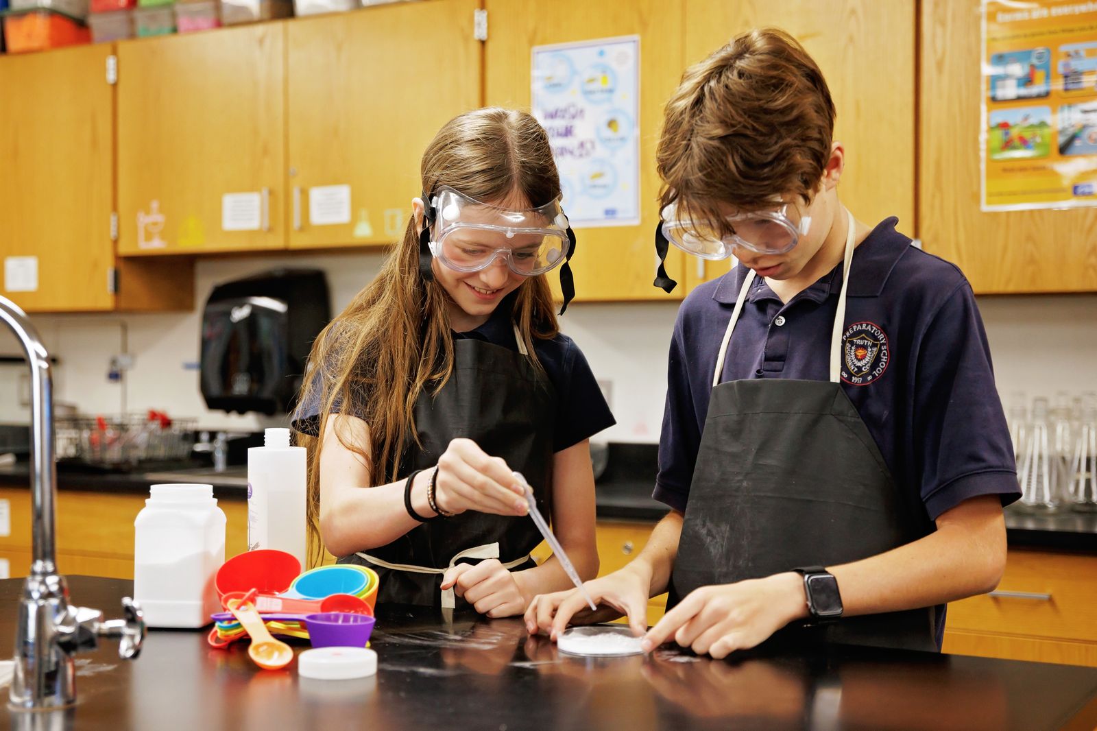 Two Valley Prep middle school students run a chemistry experiment in goggles and aprons