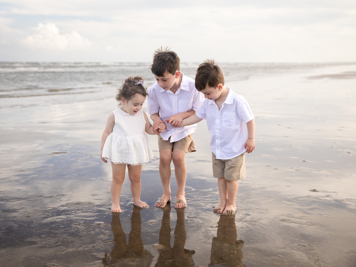 Three children looking down together on the wet sand