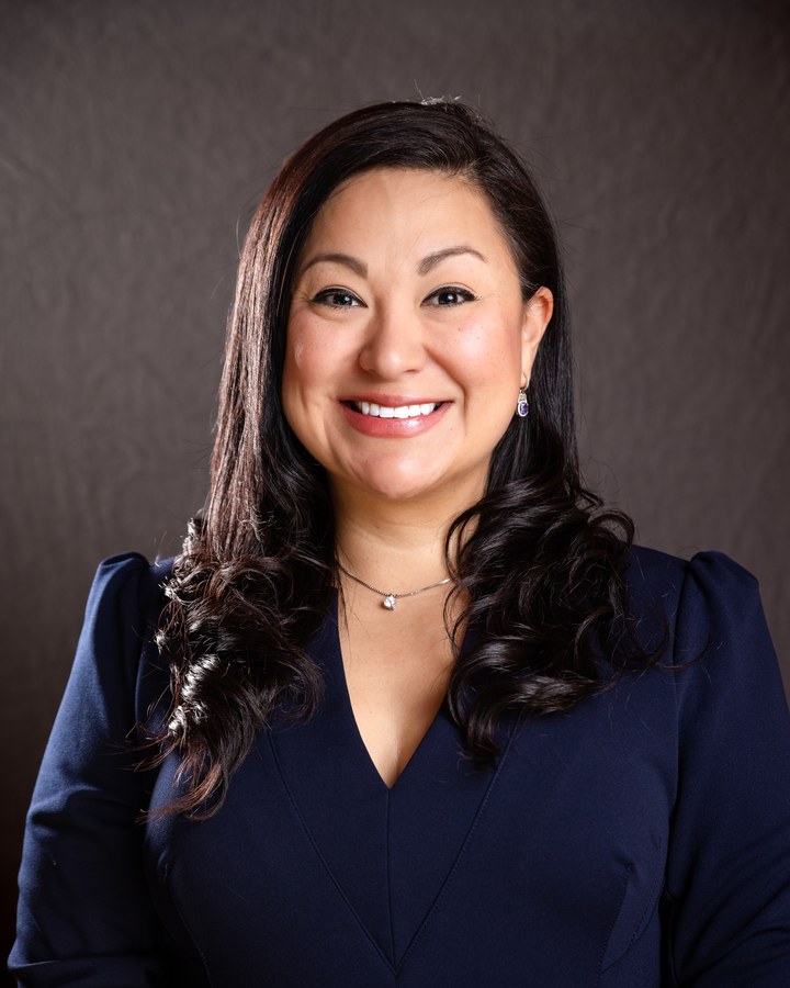 Professional headshot of a smiling woman with dark hair, blue top and silver pendant — Houston business headshot