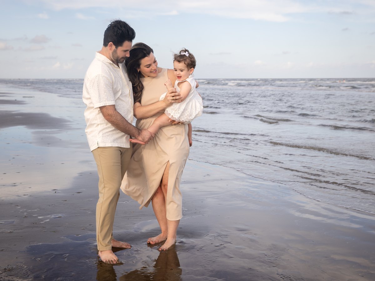 Family of three on the beach, child pointing up at the sky