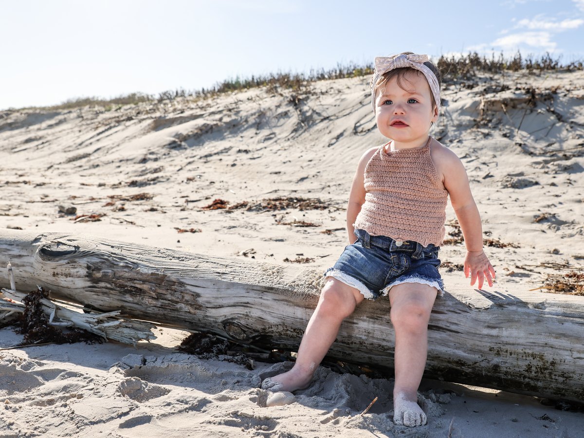 Baby sitting on a piece of driftwood on the beach