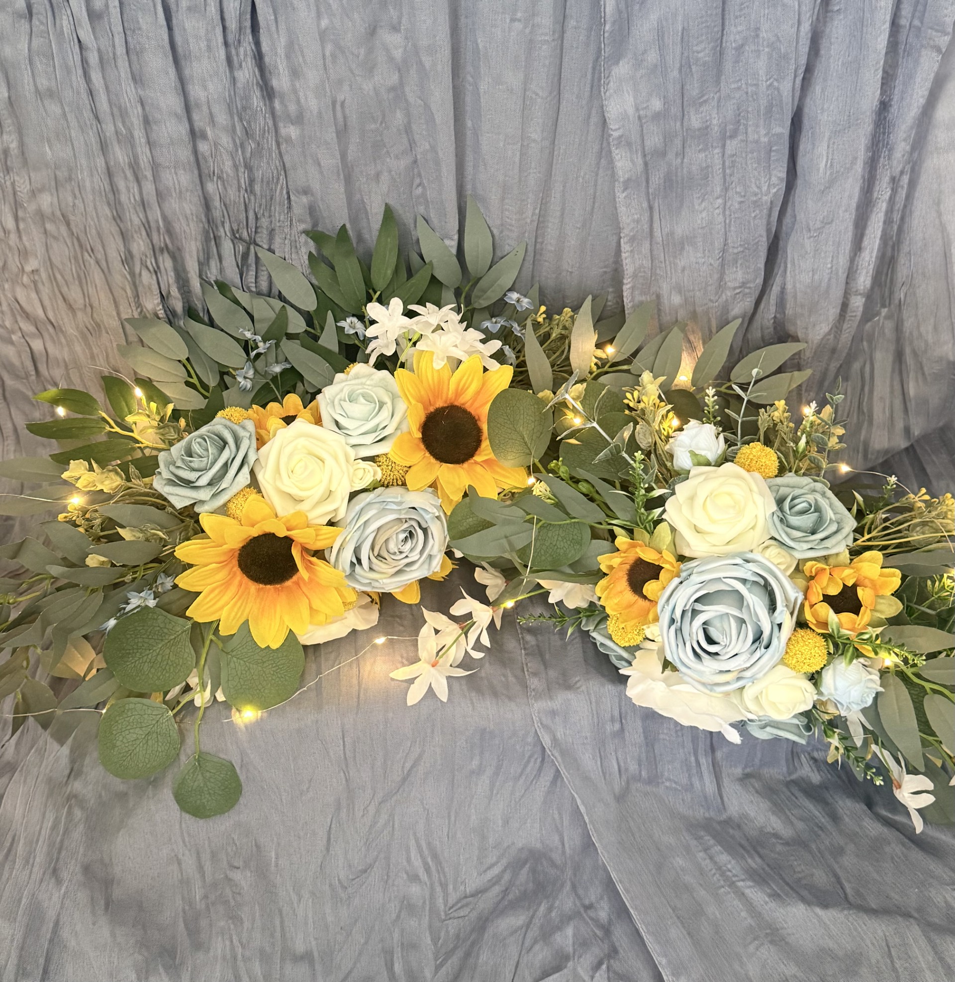 Ceremony arch florals with sunflowers, dusty blue roses, white roses, eucalyptus, and fairy lights by Petal Essence in Dallas-Fort Worth