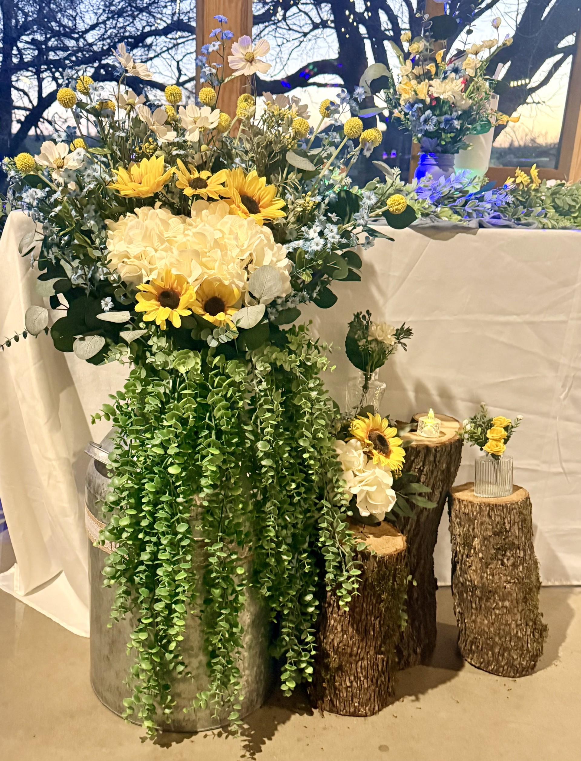 Floor arrangement with sunflowers, hydrangeas, cascading greenery in galvanized bucket with rustic wood stumps at DFW wedding venue