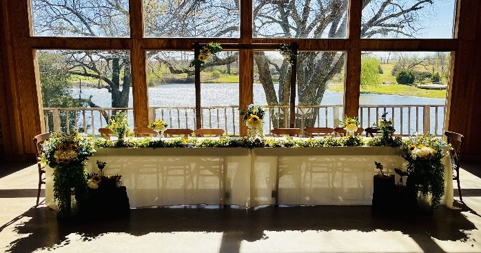 Head table setup with sunflower floral garland, greenery, and rustic accents overlooking lake at DFW wedding venue by Petal Essence