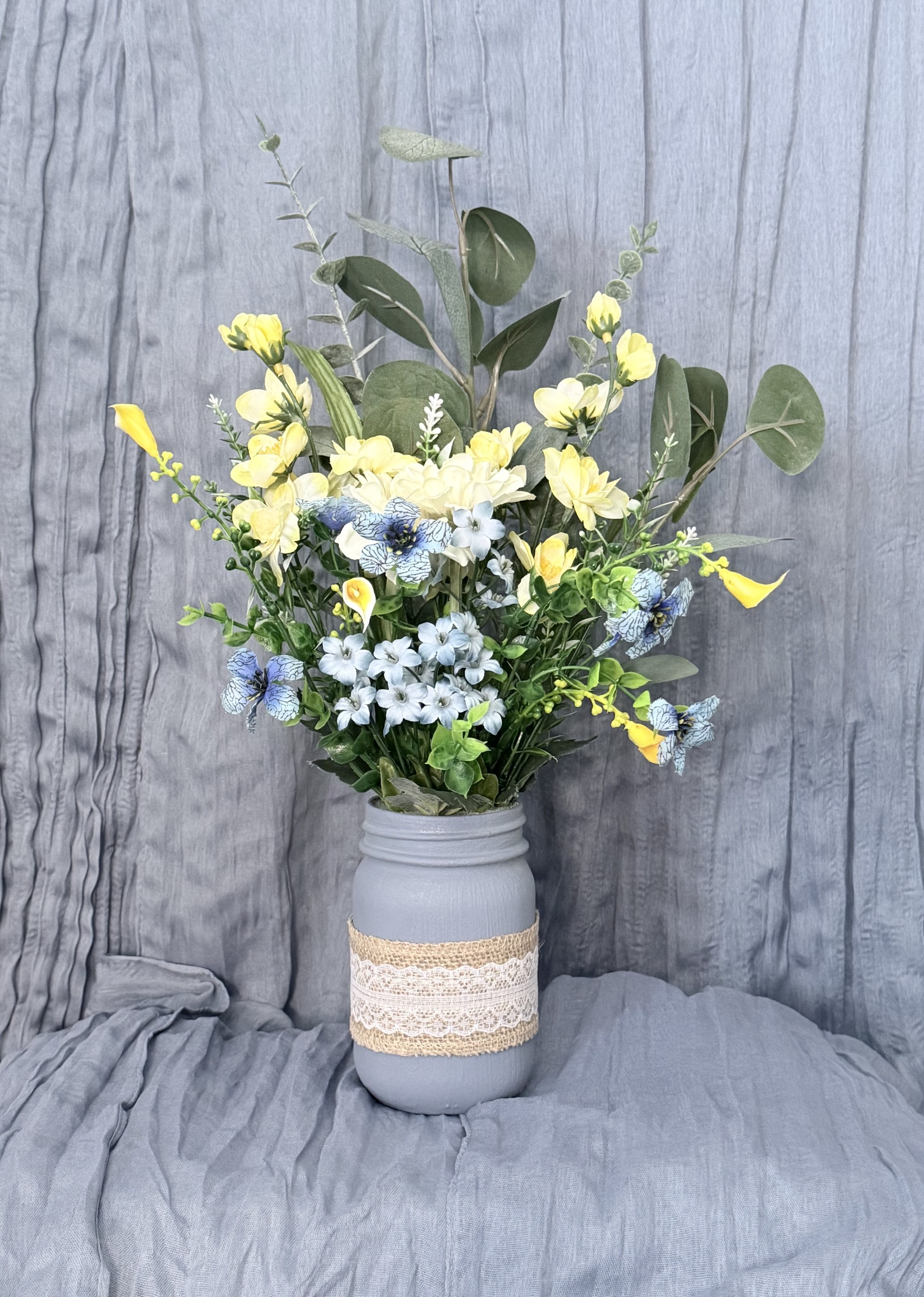 Table centerpiece arrangement with yellow freesia, blue hydrangea, calla lilies, and eucalyptus in burlap-lace mason jar by Petal Essence in DFW