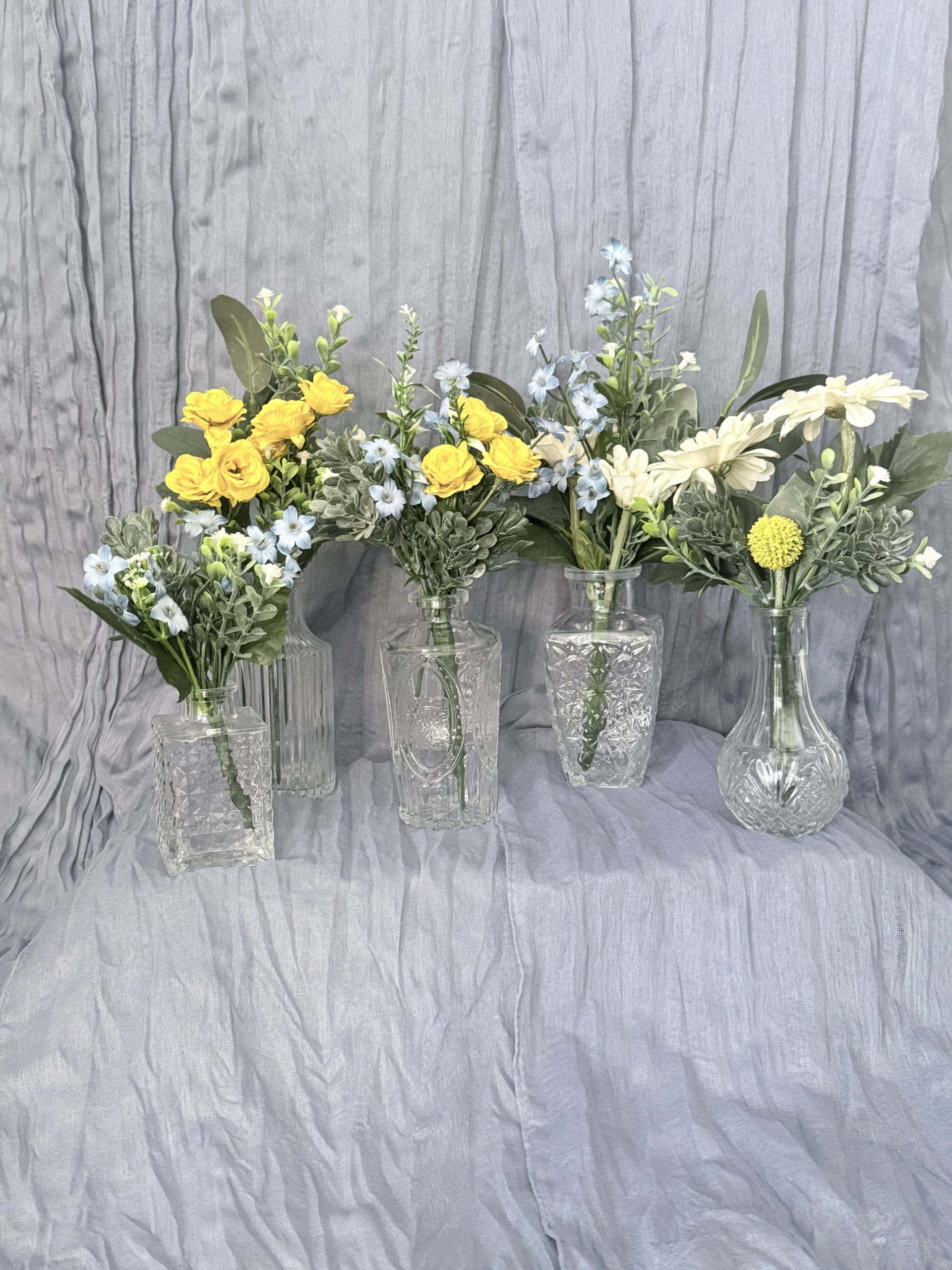 Bud vase arrangements with yellow roses, blue delphinium, daisies, and greenery in vintage glass vases by Petal Essence in Dallas-Fort Worth