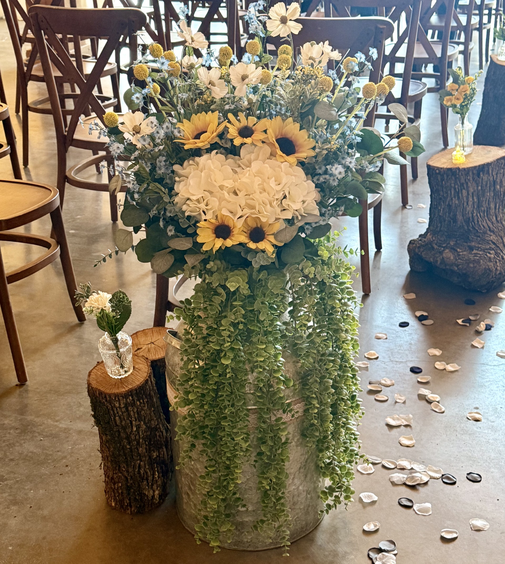 Ceremony aisle floor arrangement with sunflowers, hydrangeas, cosmos, cascading greenery, and scattered petals by Petal Essence in Dallas-Fort Worth