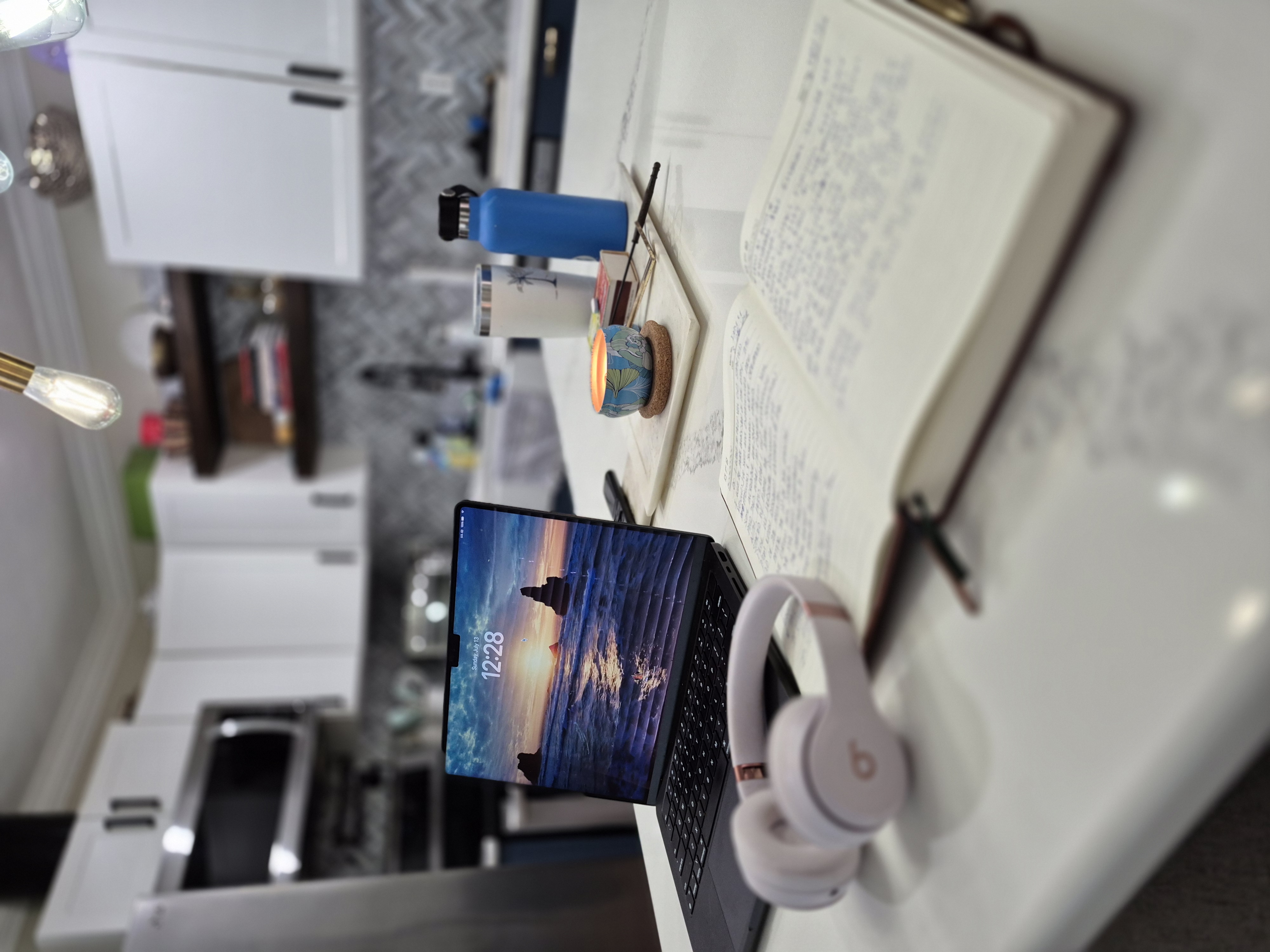 Trish's real workspace β laptop, journal, headphones, candle, and coffee