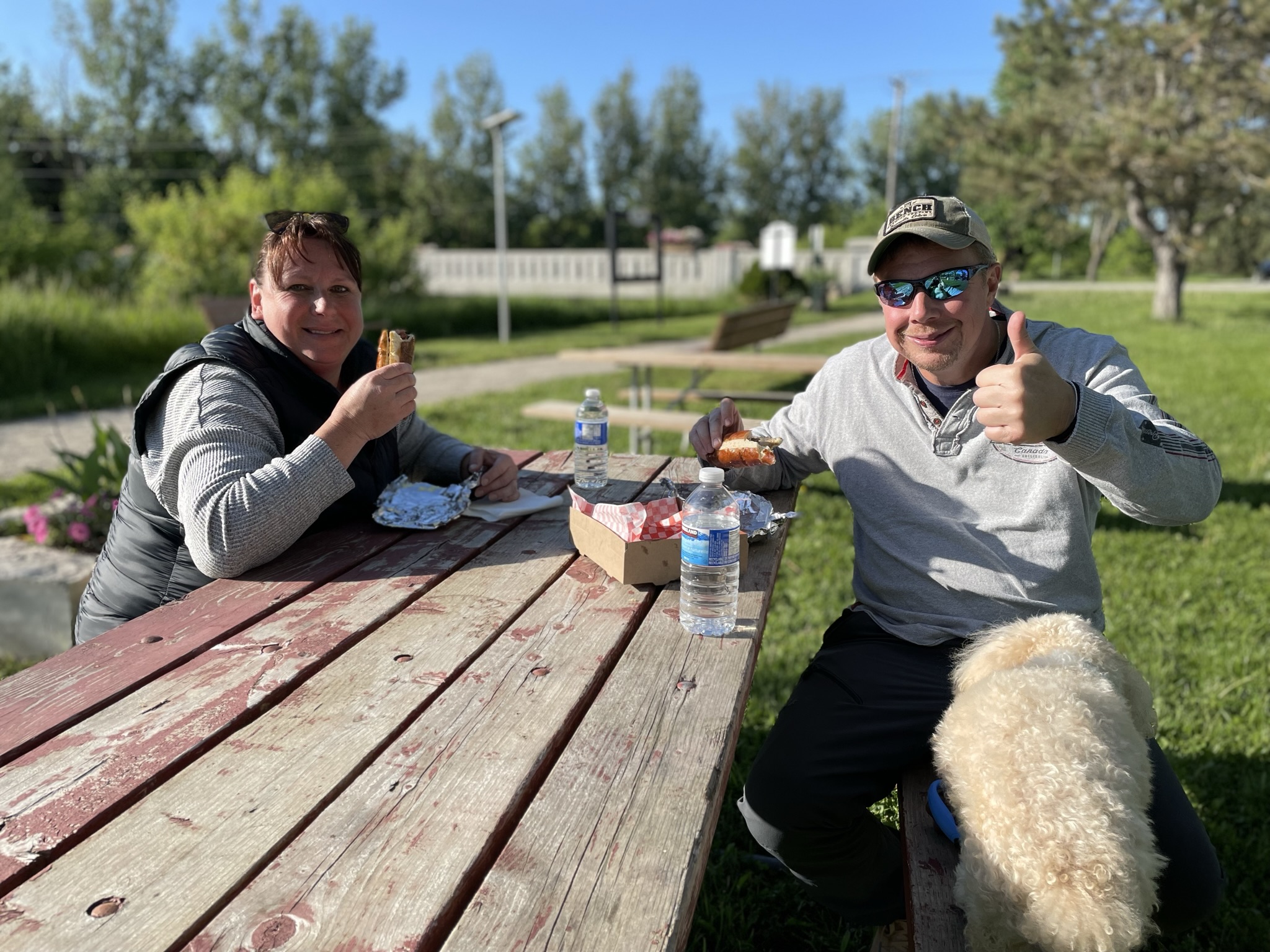 Couple with thumbs up and their dog at picnic table