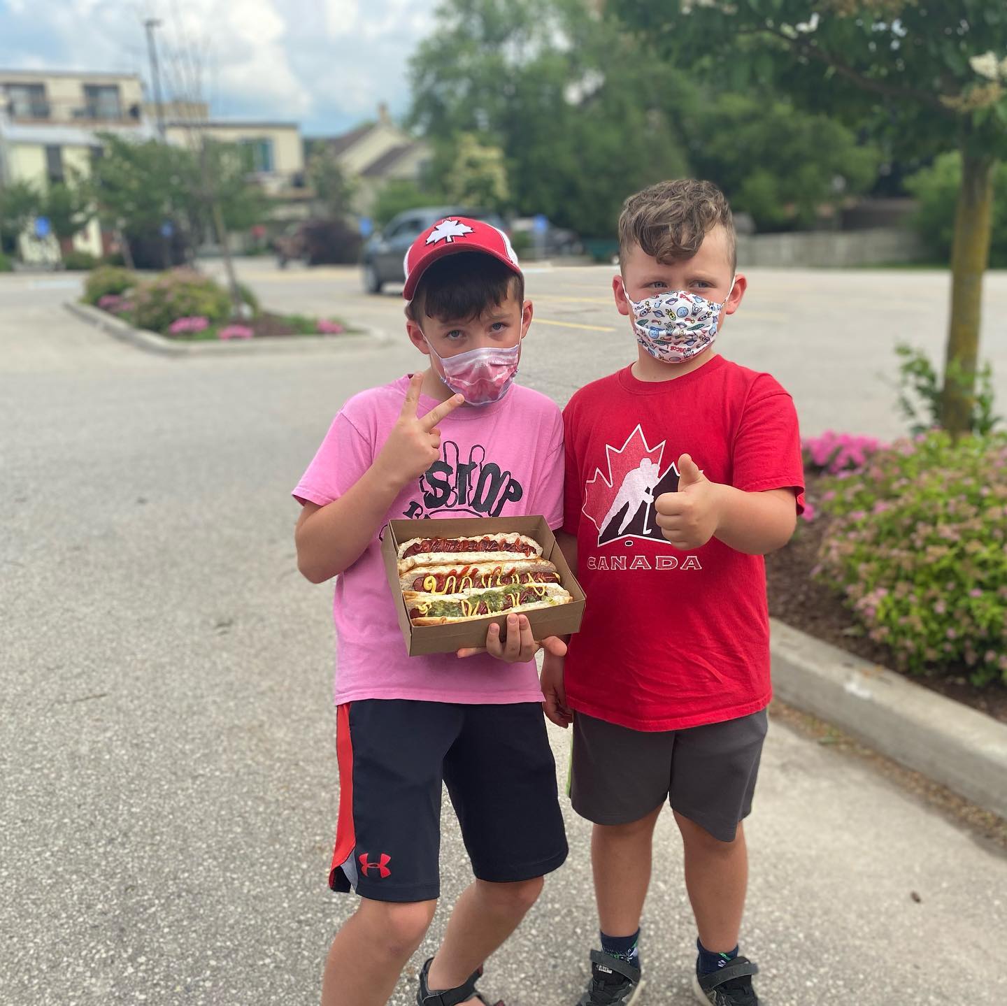 Two kids with a box of loaded hot dogs giving thumbs up