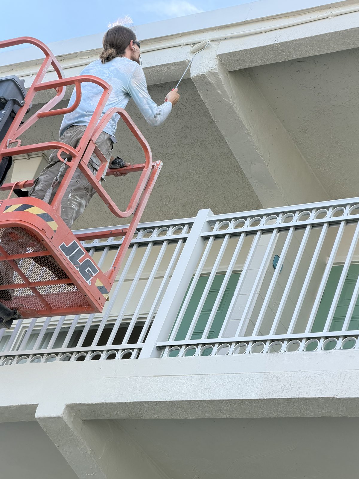 Legacy Surface Prep crew member rolling coating from a lift above a freshly coated white railing