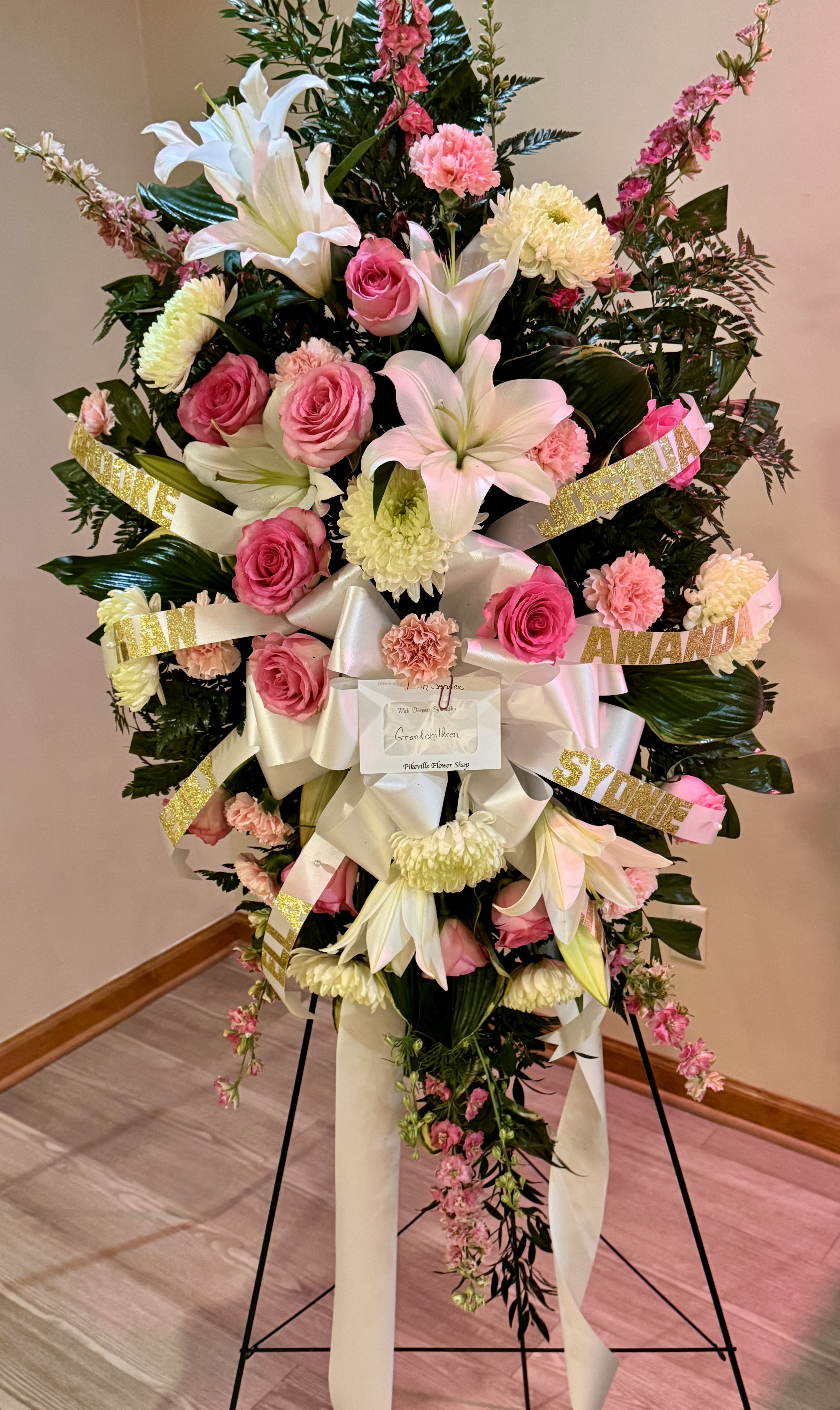 Personalized grandchildren standing spray with pink roses, lilies, and gold name ribbons