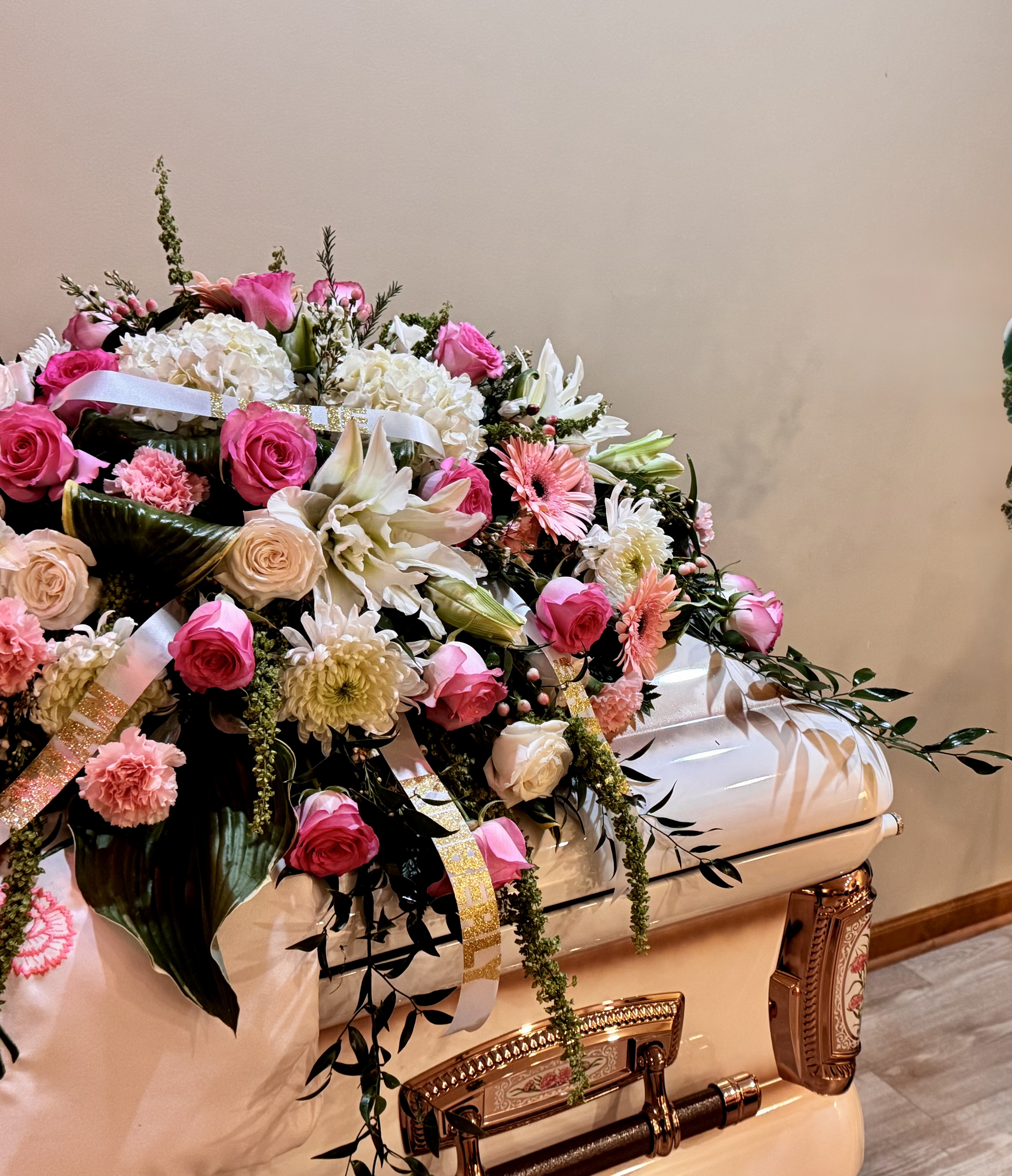 Pink roses, white hydrangeas, and gerbera daisies casket spray with gold ribbon