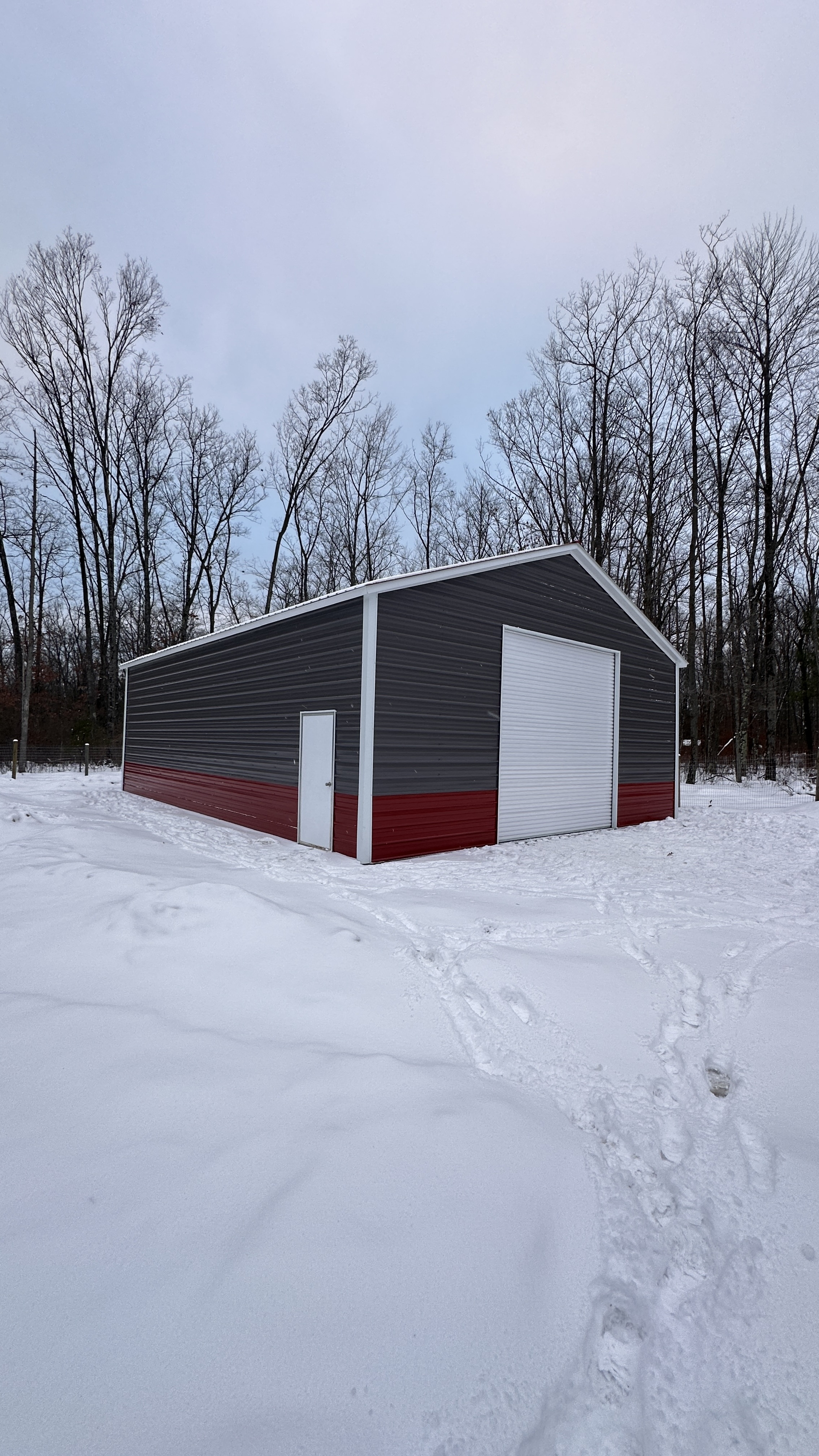 Dark gray and burgundy two-tone steel building with white roll-up door in winter