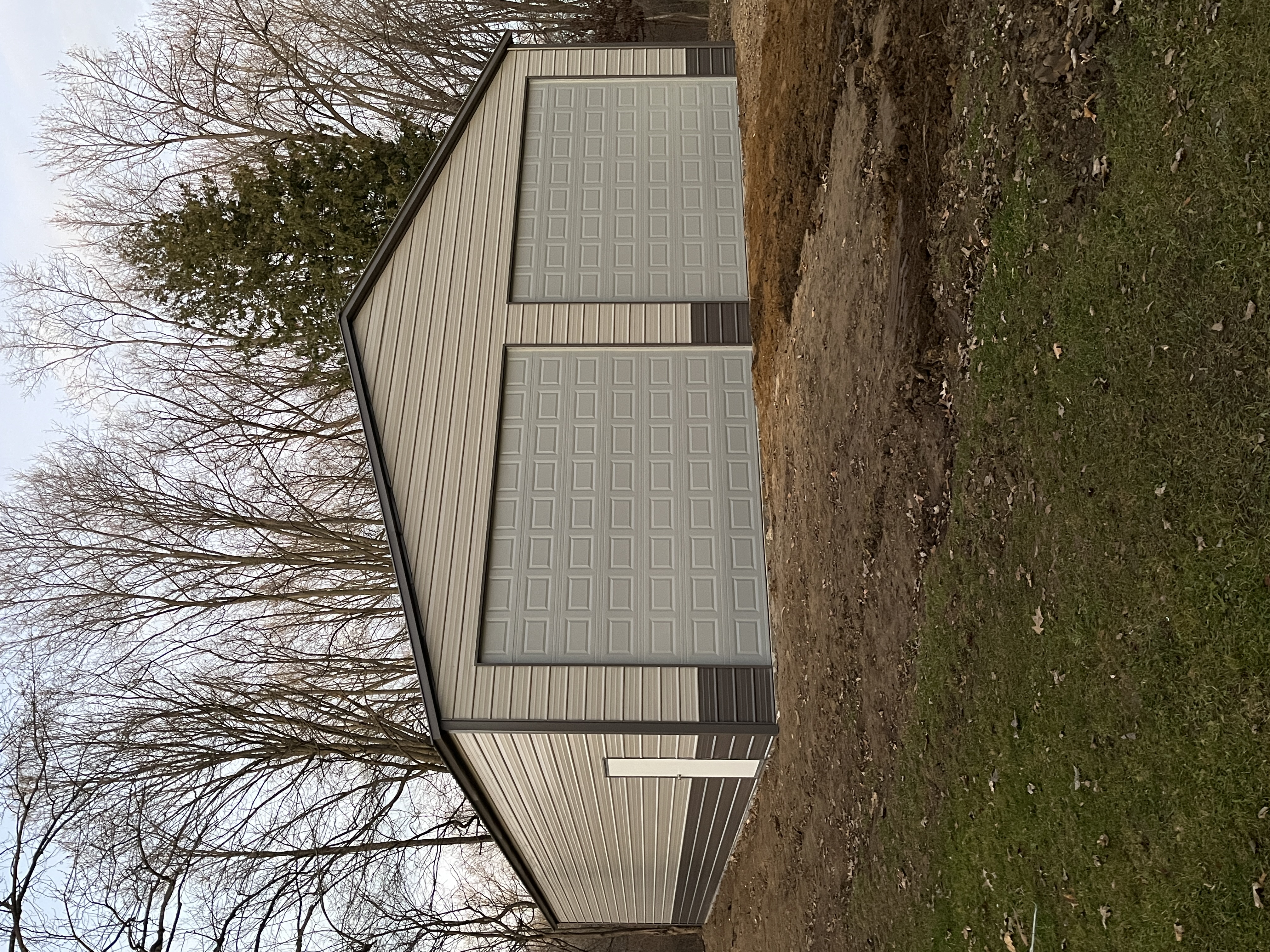 Light gray steel building with two large garage doors and dark trim on green grass