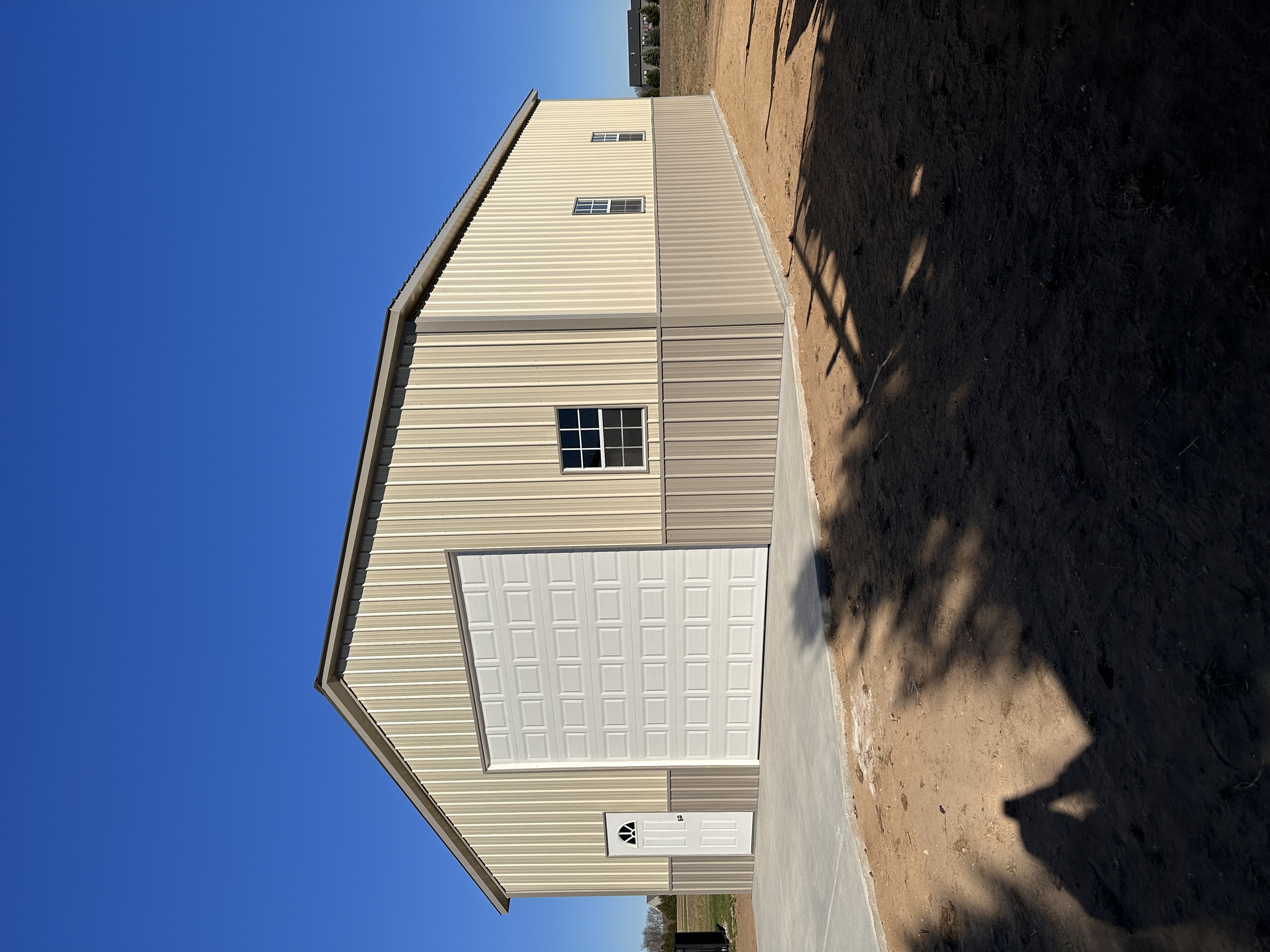 Large tan steel building with oversized garage door and windows under clear blue sky