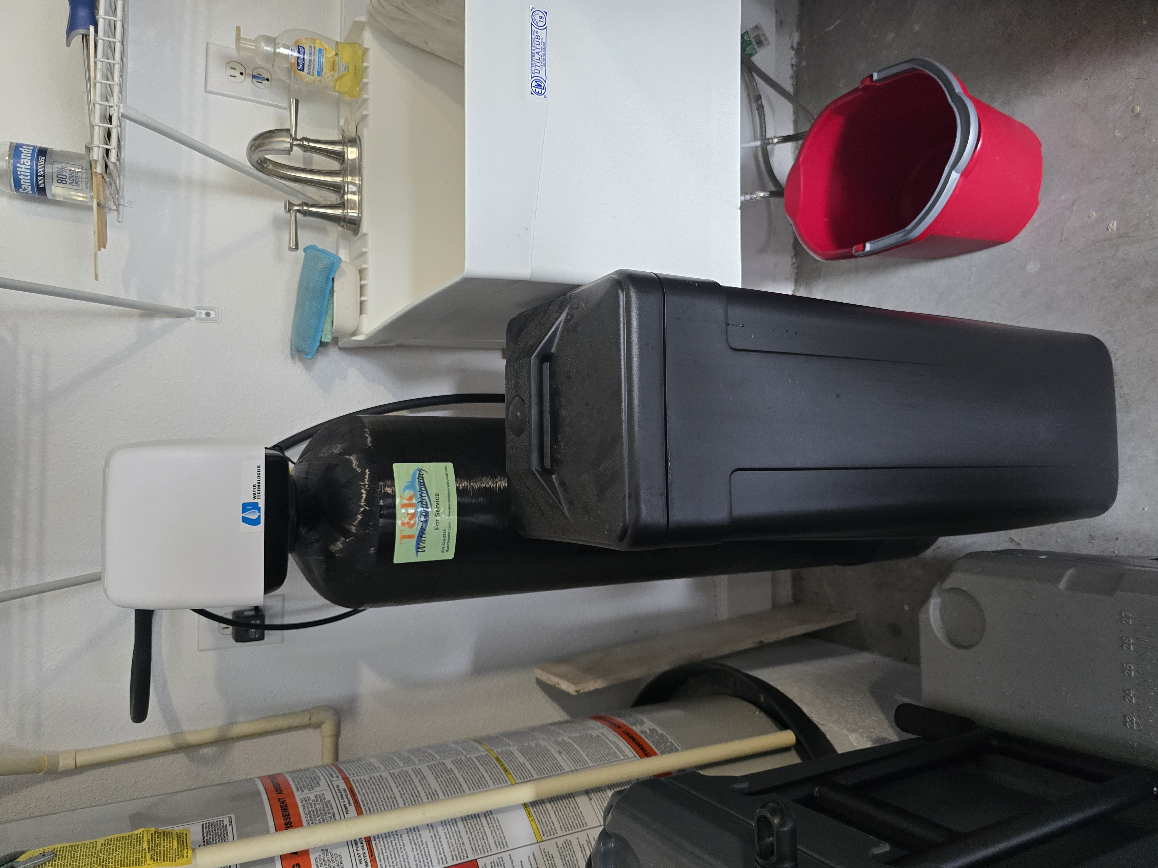 T&K Water Conditioning black water softener with salt tank installed in utility room next to sink