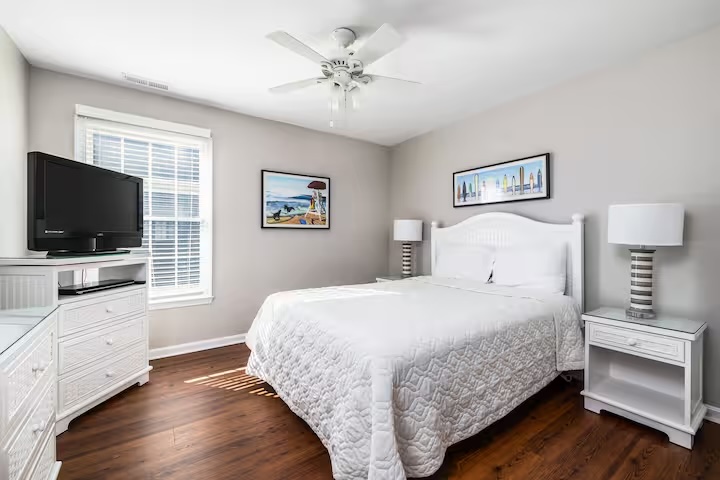 White bedroom with beach art ceiling fan and hardwood floors