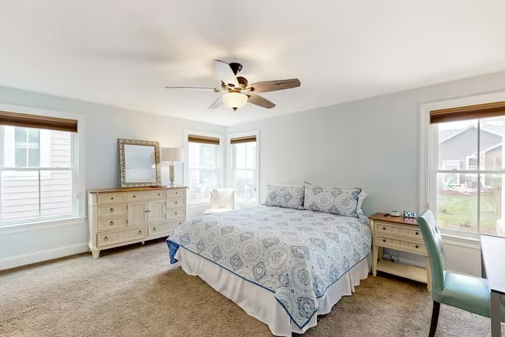 Spacious master bedroom with ceiling fan dresser and garden views