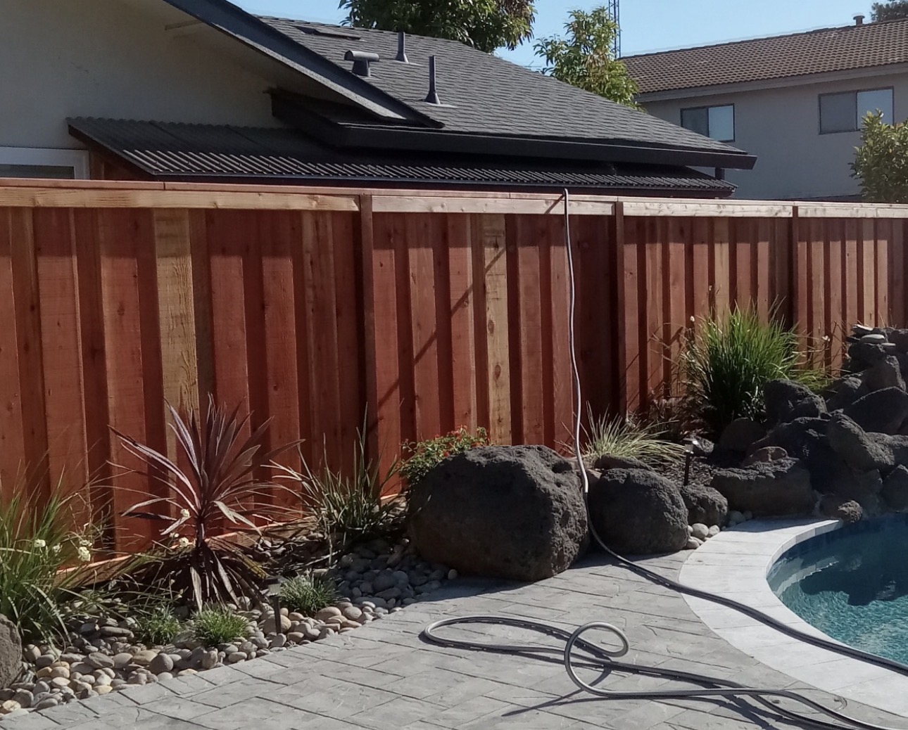 Redwood privacy fence installation alongside pool with landscaping