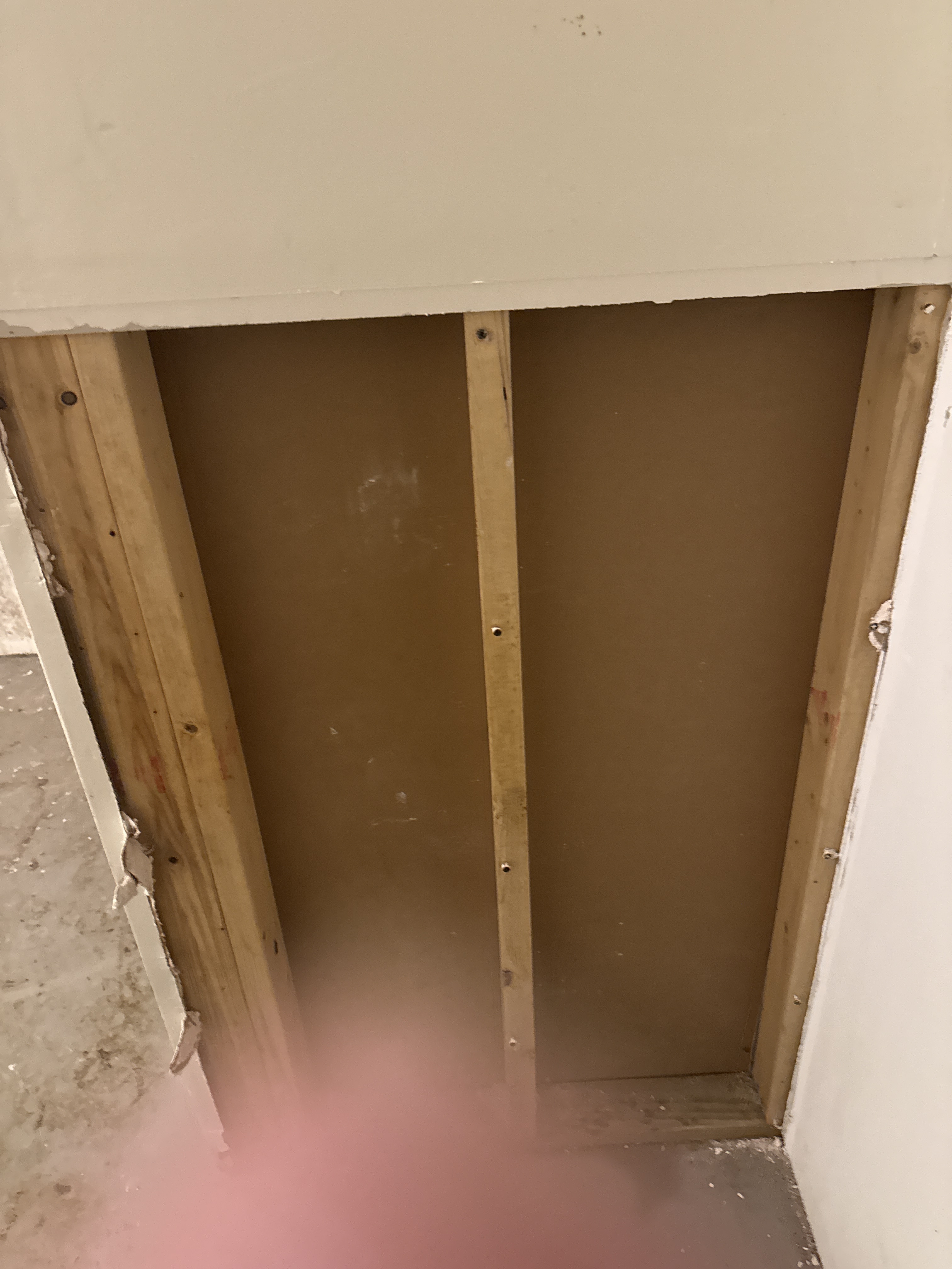 Opened wall cavity in a basement showing framing and the wall behind it