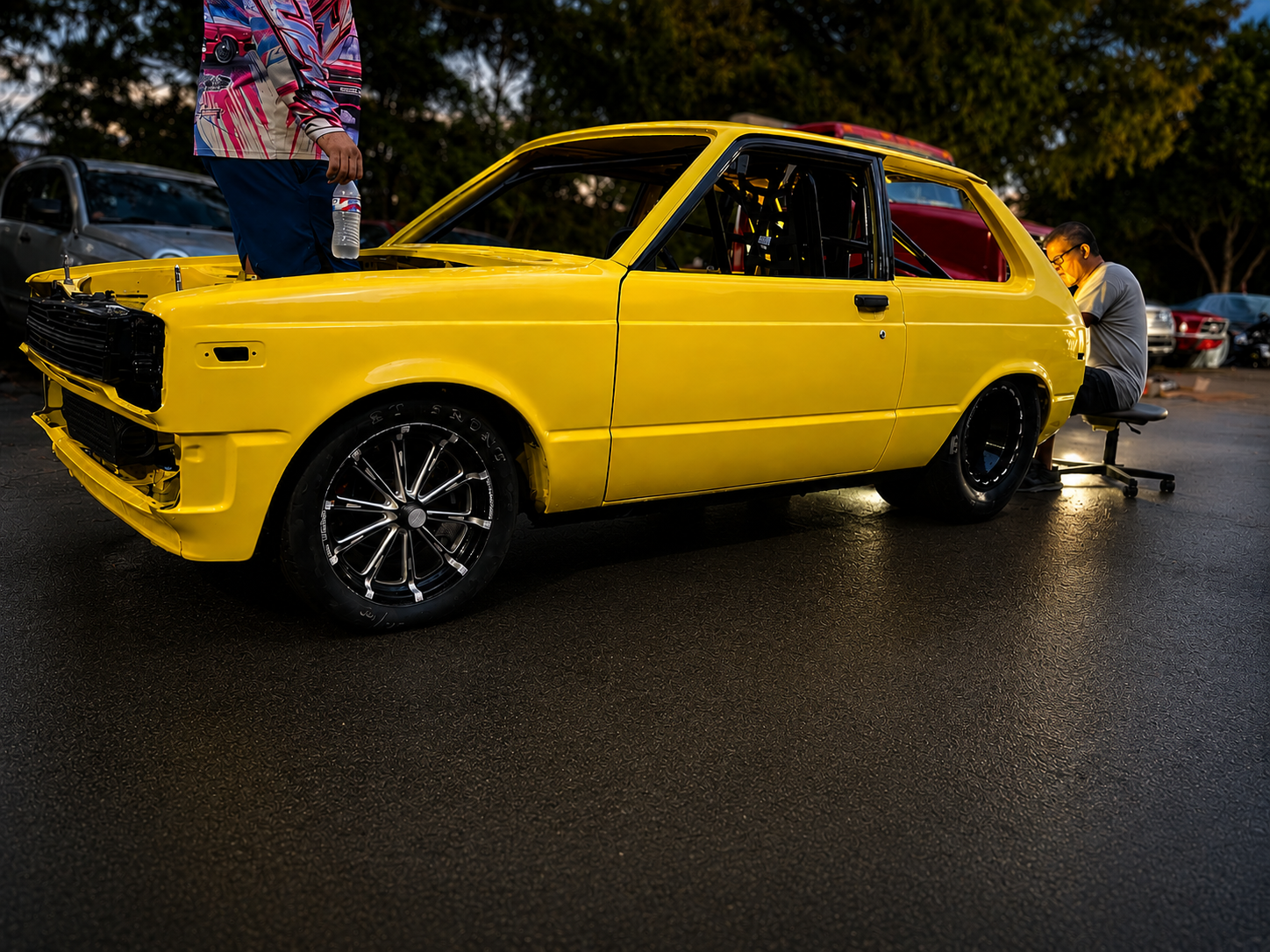 Yellow race car at car meet showing roll cage and custom wheels