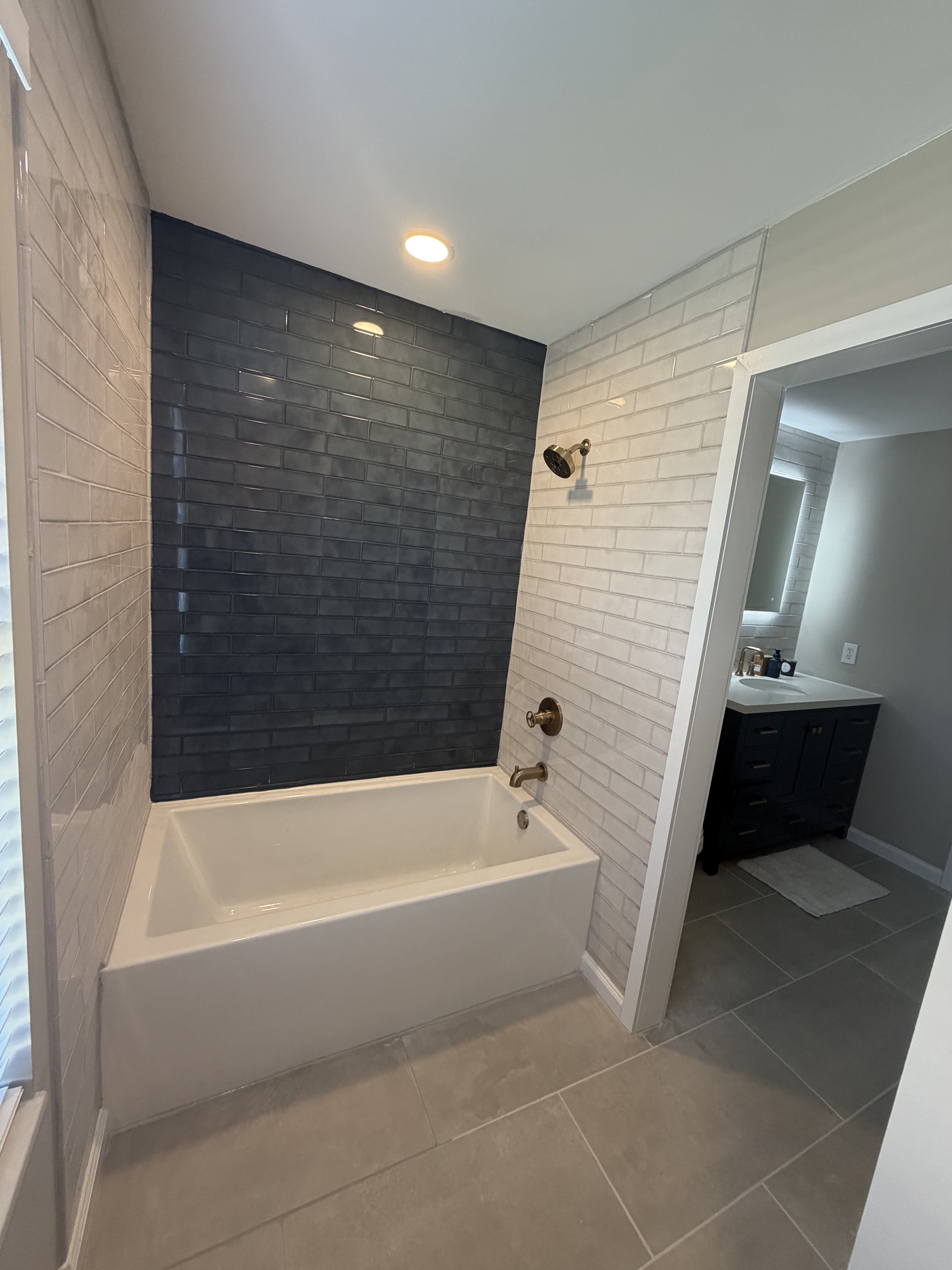Full bathroom view with navy accent tile wall, soaking tub, subway tile, and navy vanity