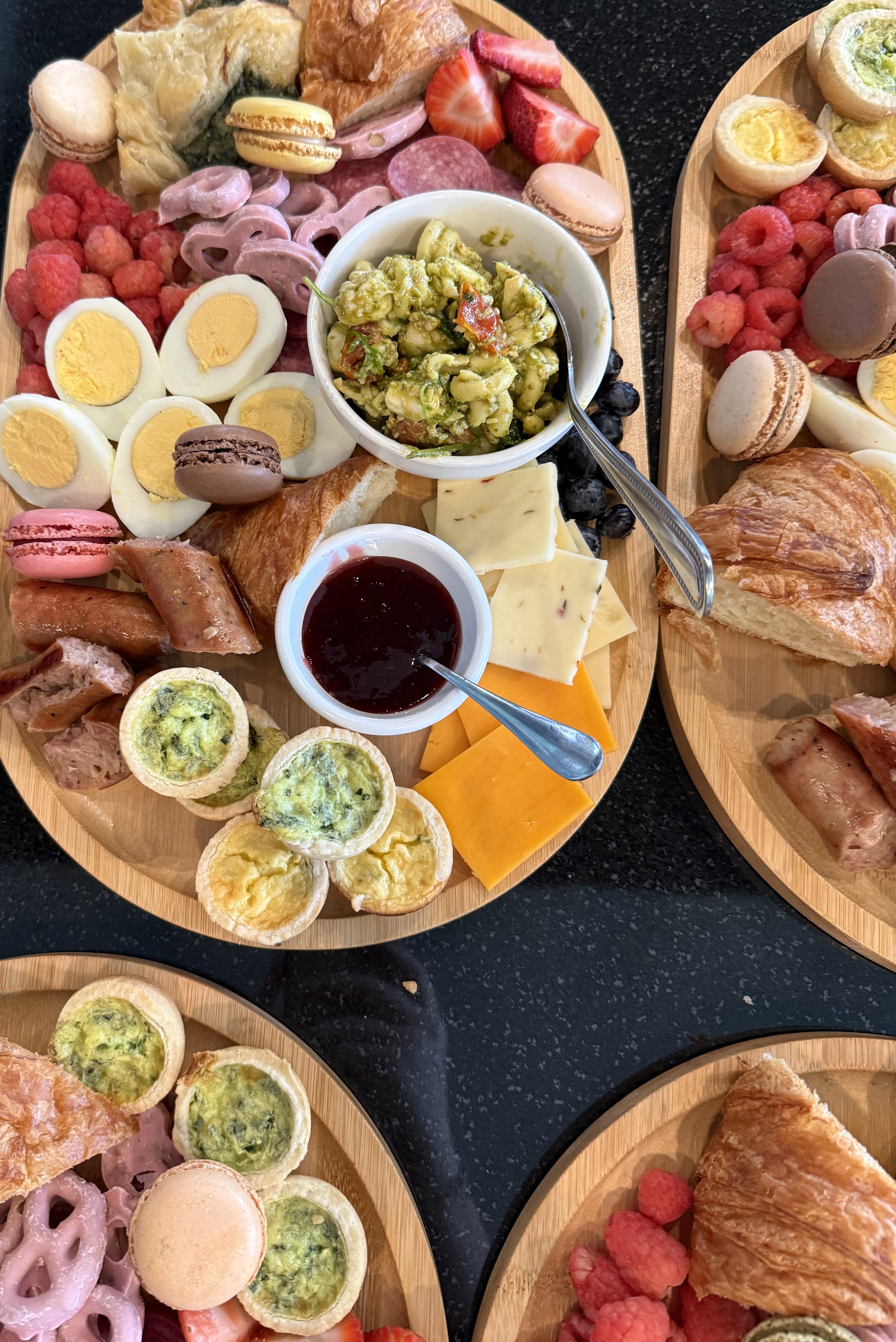 Brunch boards with quiche bites, eggs, croissants, macarons, and pesto pasta salad
