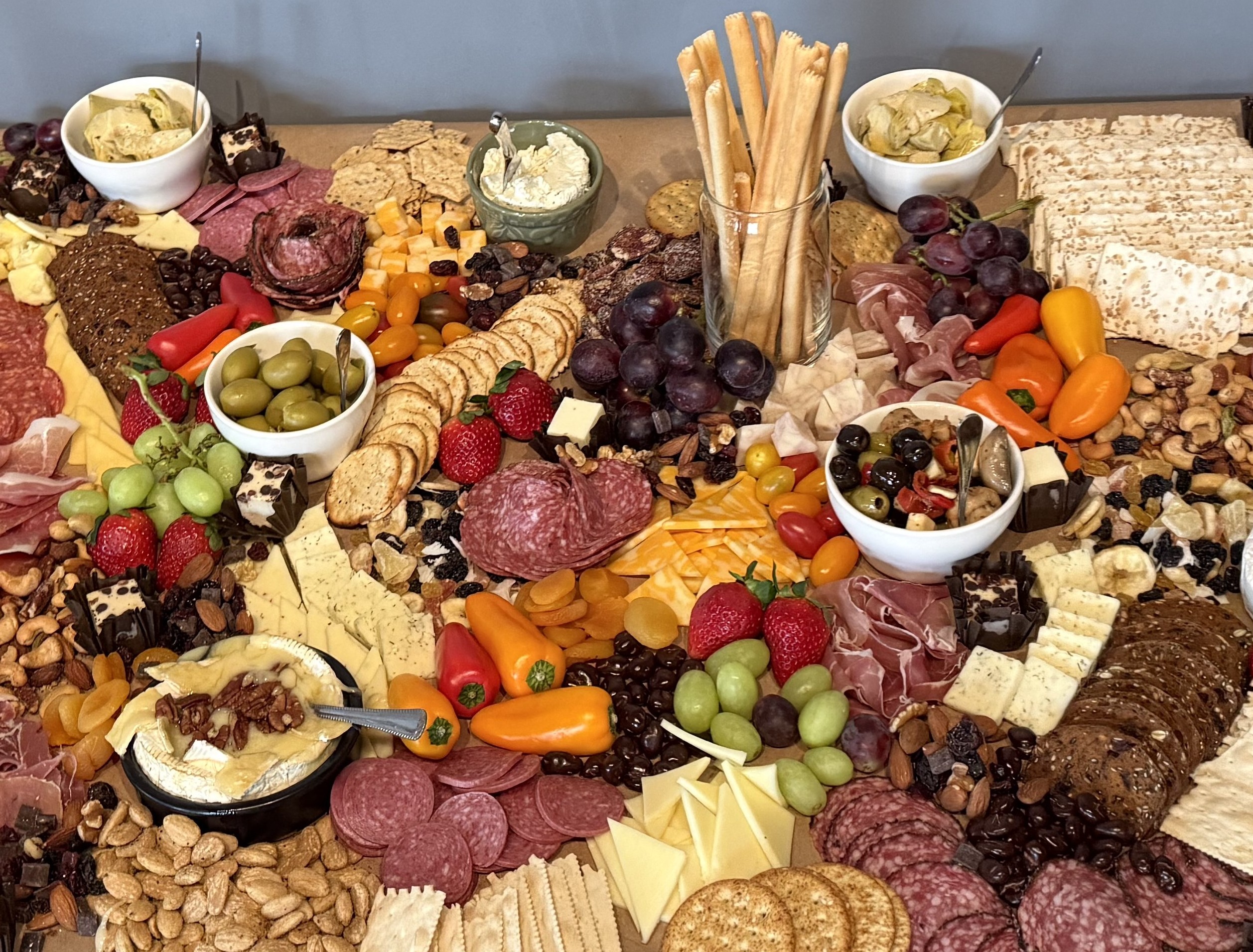 Massive grazing table with salami, cheeses, olives, breadsticks, peppers, and nuts