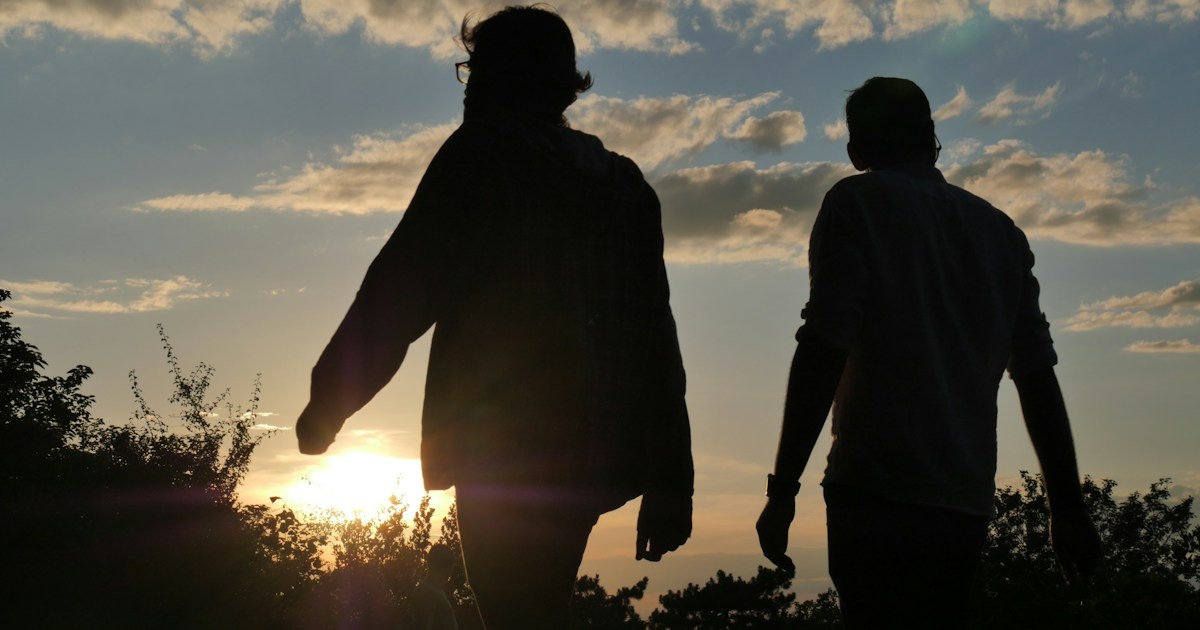 Two men walk side by side toward the setting sun