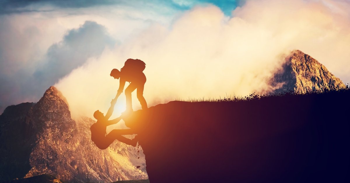 One man reaching down to pull another up over a cliff edge — brotherhood that holds the line