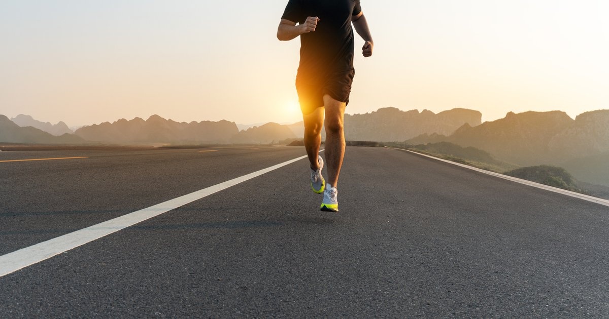 A man running toward the viewer on an empty road at golden light — steady endurance, holding the line