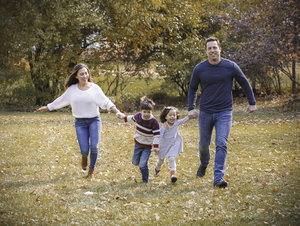 Family of four holding hands and running through autumn leaves — IDT Photo fall portrait