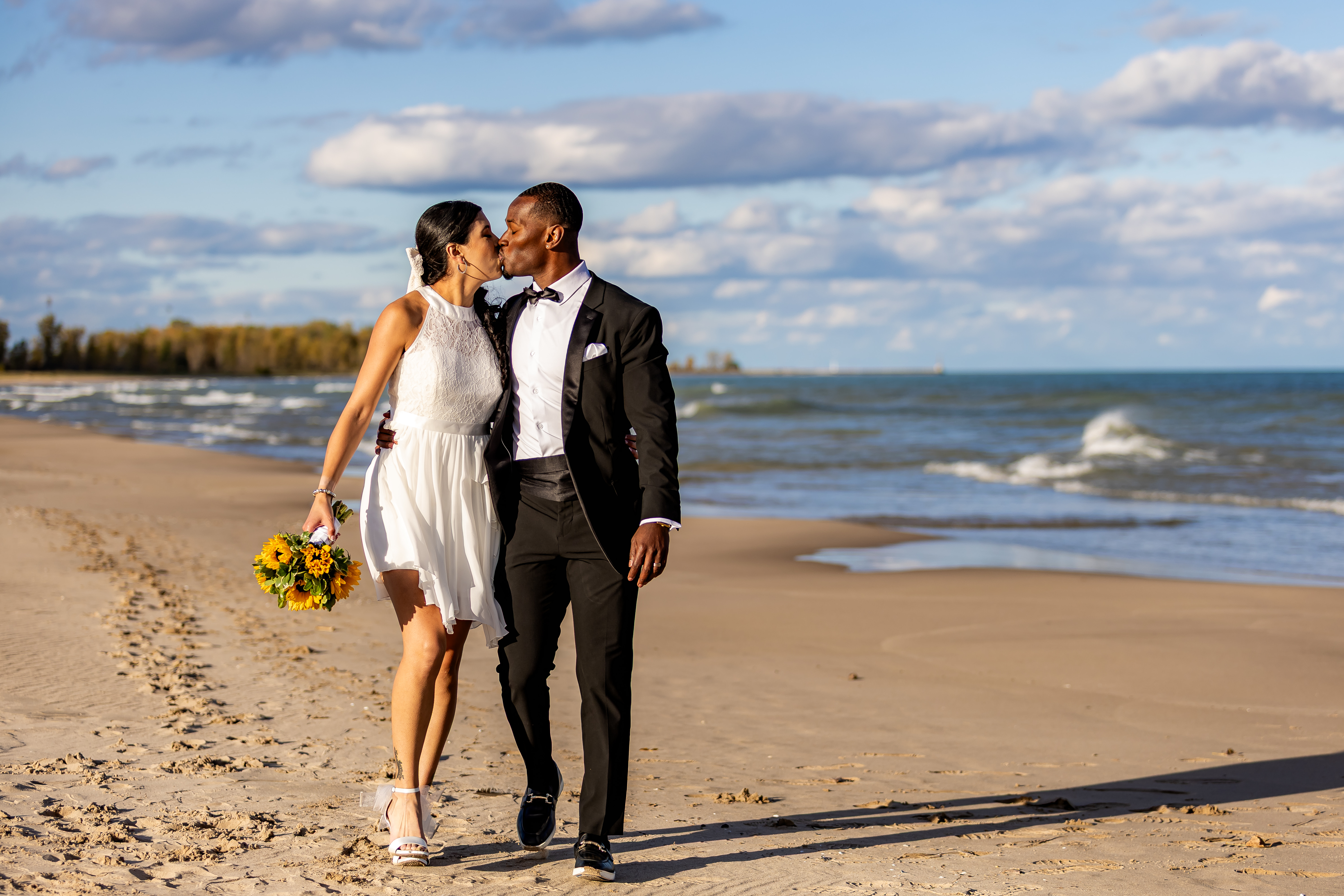 Bride and groom kissing mid-stride on Lake Michigan beach with dramatic clouds and waves — IDTPhoto wedding photography