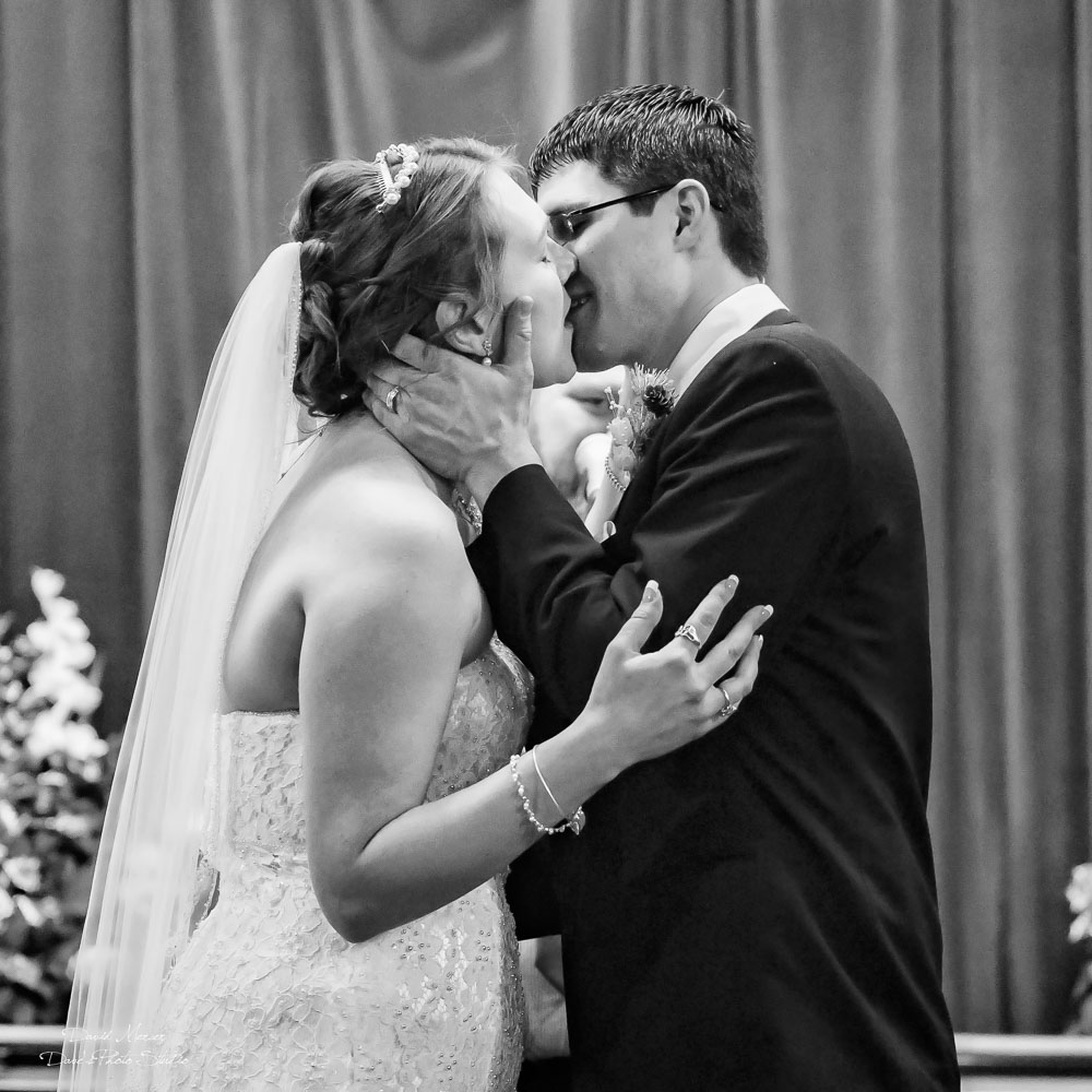 Black and white first kiss at church altar — groom cradling bride's face during ceremony — IDTPhoto wedding photography