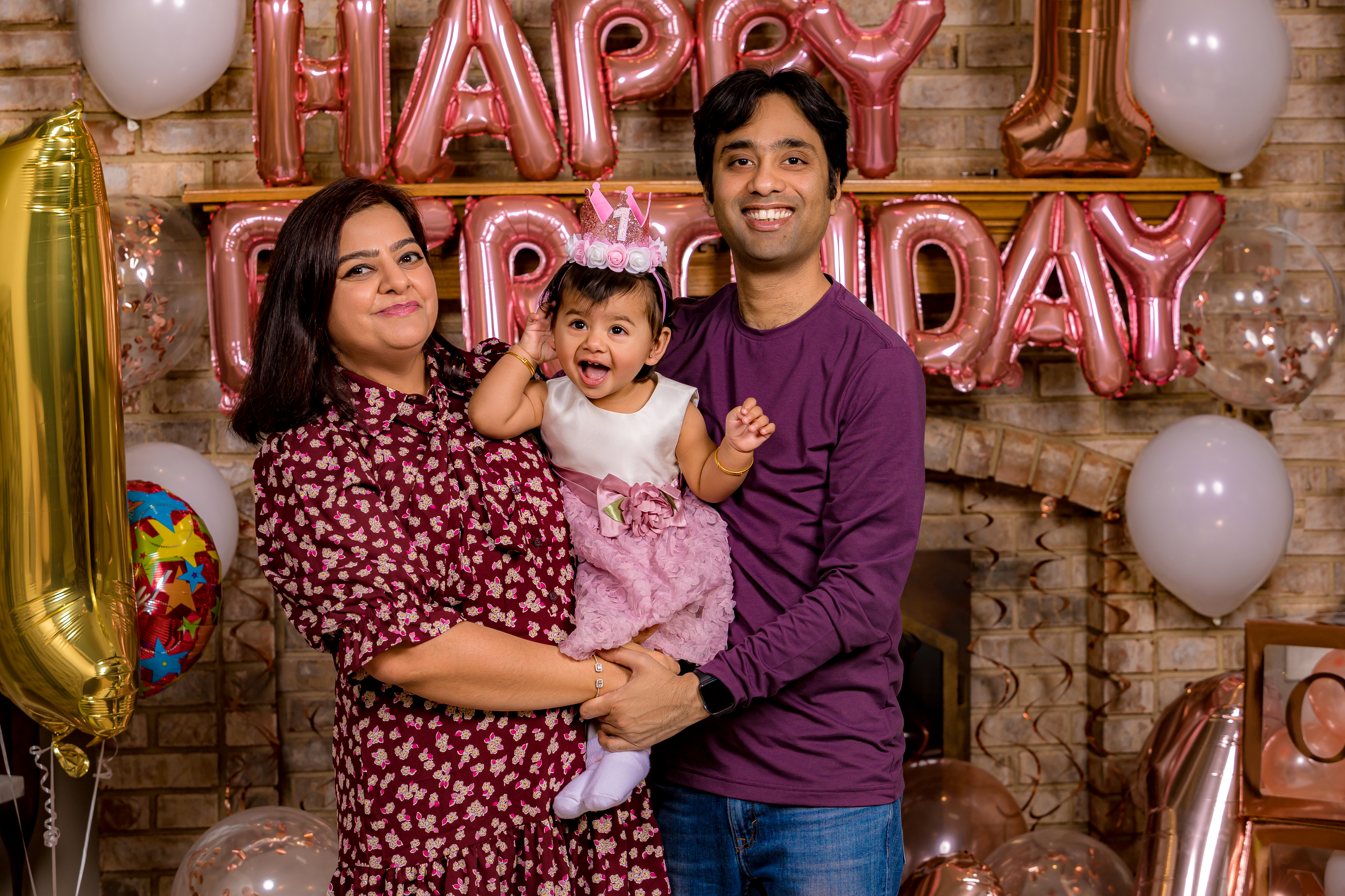 Family of three laughing together in front of Happy Birthday balloons — indoor cake smash session IDTPhoto