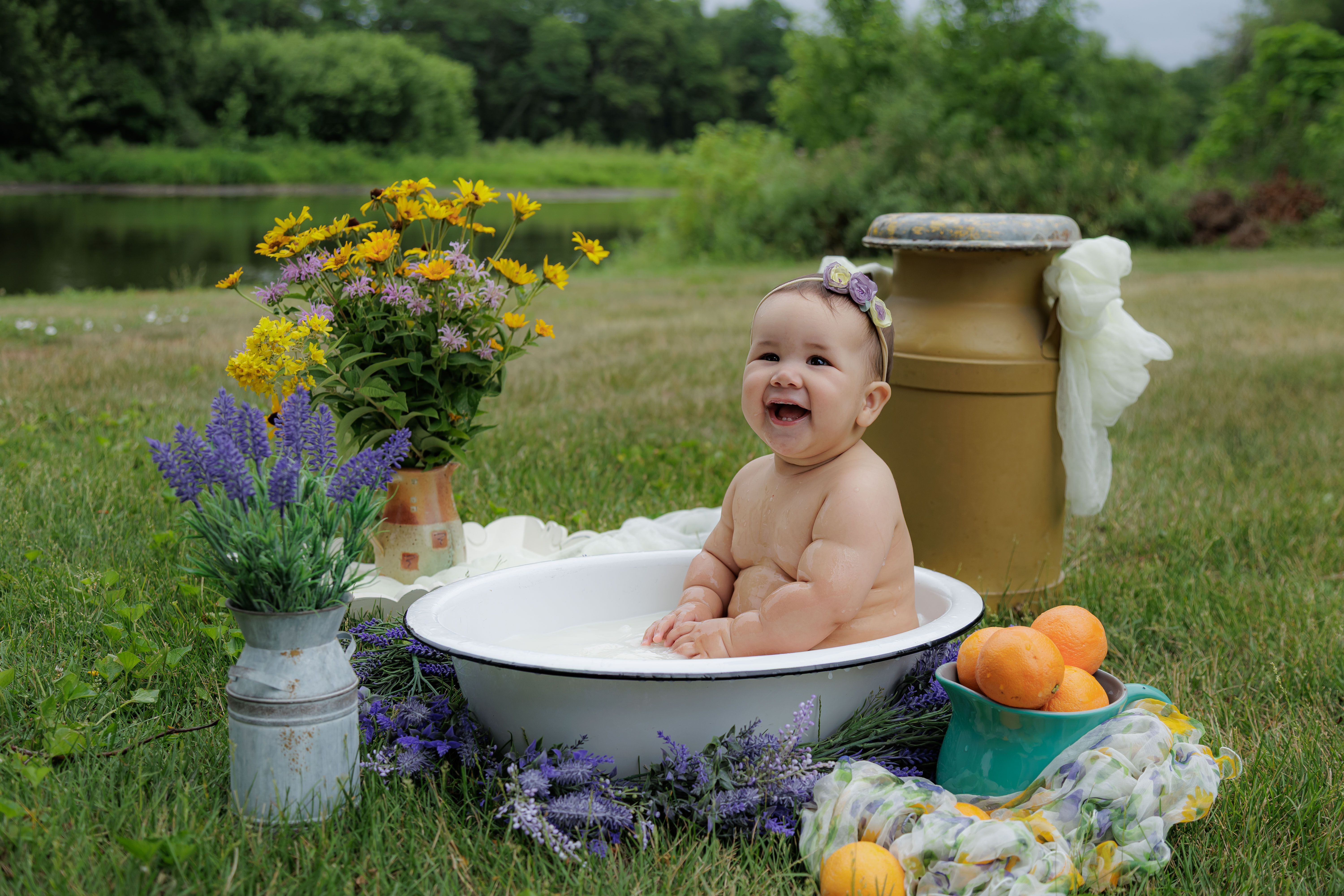 Baby laughing big while sitting in outdoor milk bath tub surrounded by yellow daisies and lavender — IDTPhoto sitter session