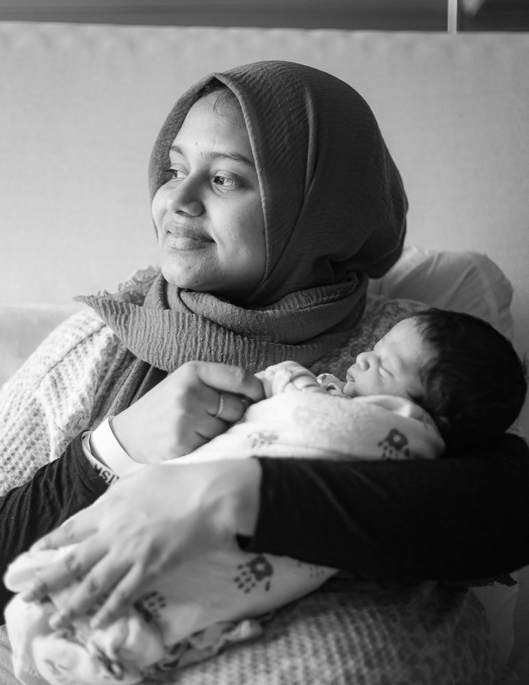 Fresh 48 black & white — mom in hijab gazing down at sleeping newborn in hospital room