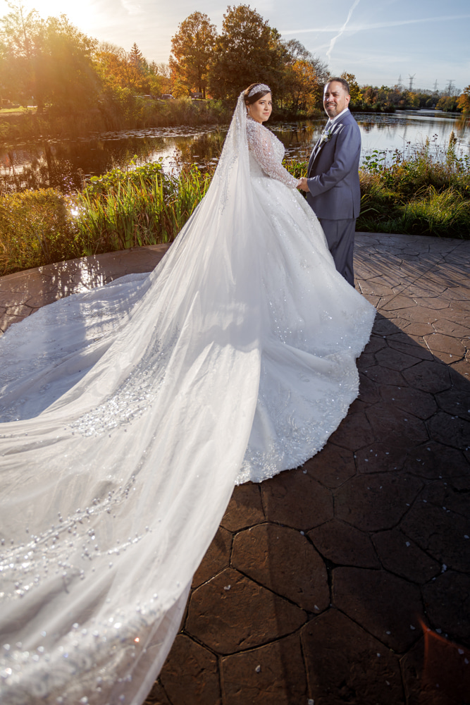 Bride's cathedral veil and train spread across stone terrace at golden hour with pond and fall foliage — IDTPhoto wedding