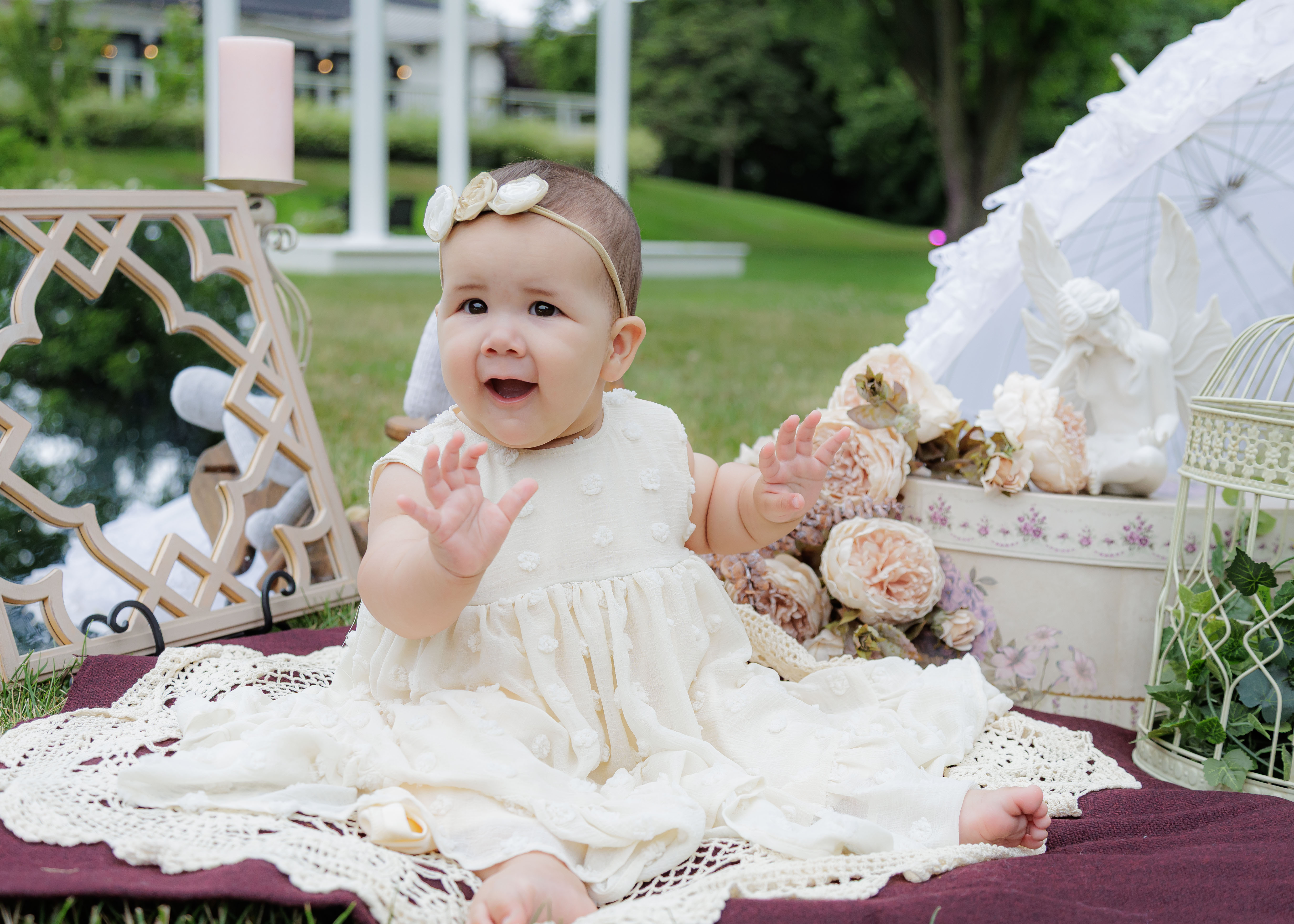 9-month baby girl clapping hands with joyful open-mouth smile during outdoor garden sitter session — IDTPhoto