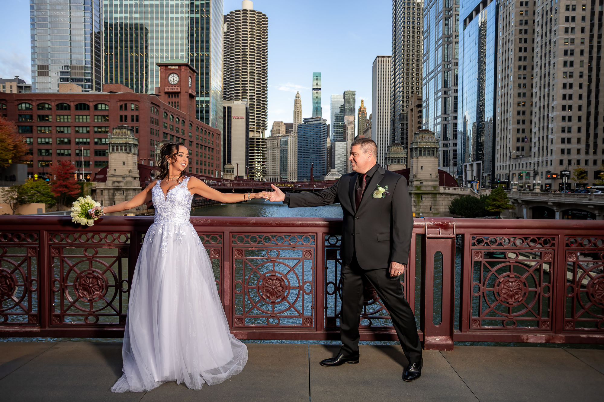 Bride and groom holding hands on Chicago Riverwalk bridge with city skyline — IDTPhoto wedding Chicagoland